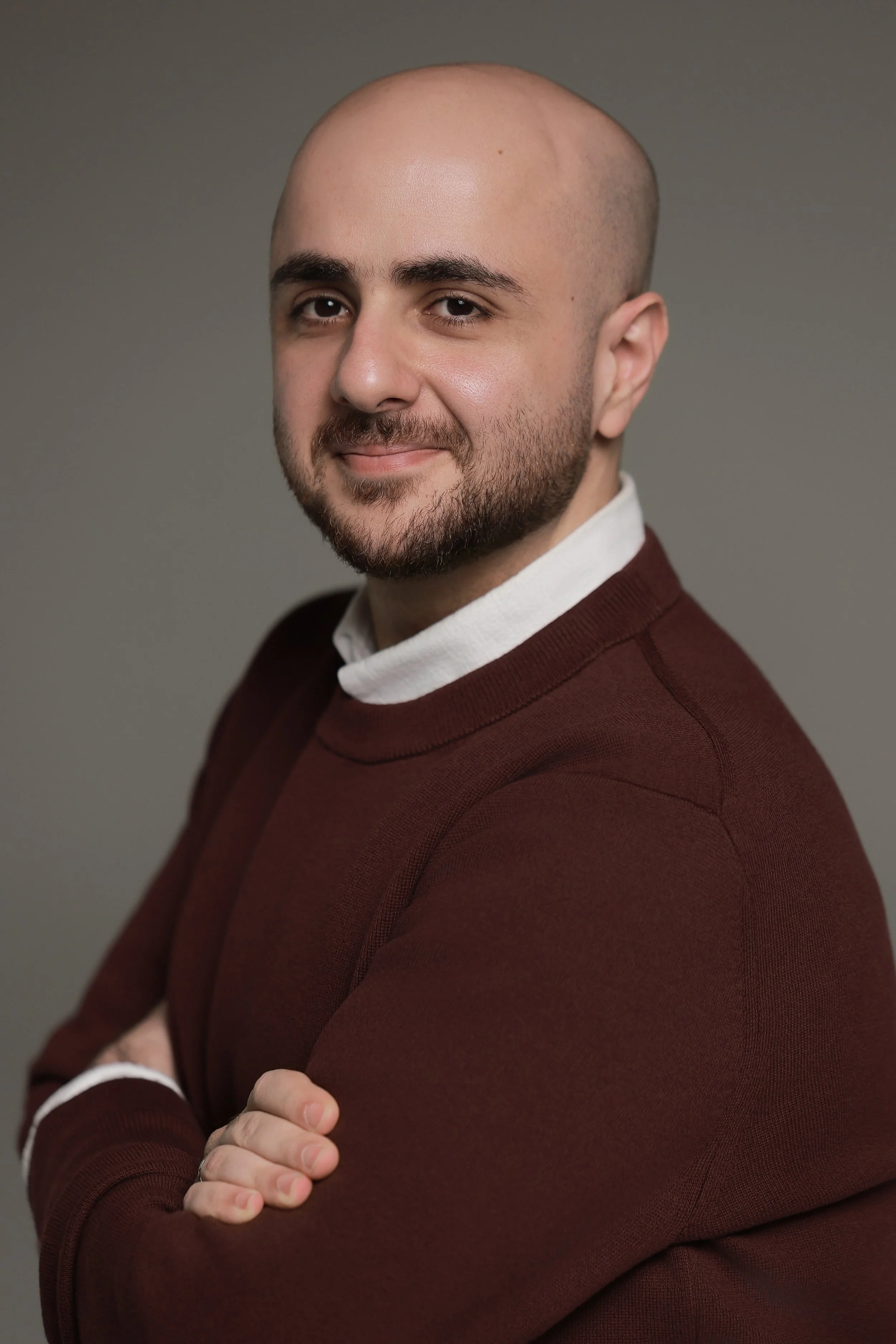Abdulmonem Ali, wearing a maroon sweater over a white shirt, is smiling slightly.