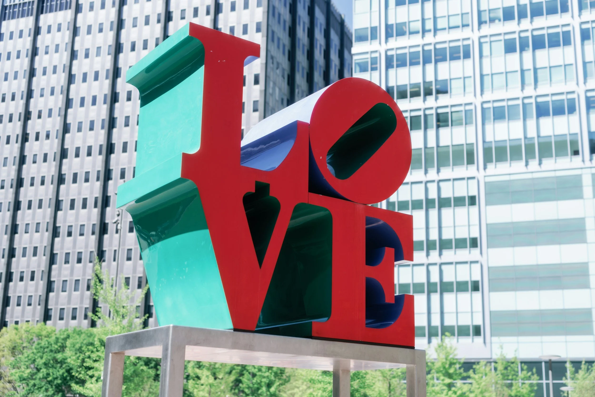 Colorful sculpture of the word "LOVE" with large, three-dimensional letters in green, red, purple, and white, set outdoors in front of a modern glass office building.