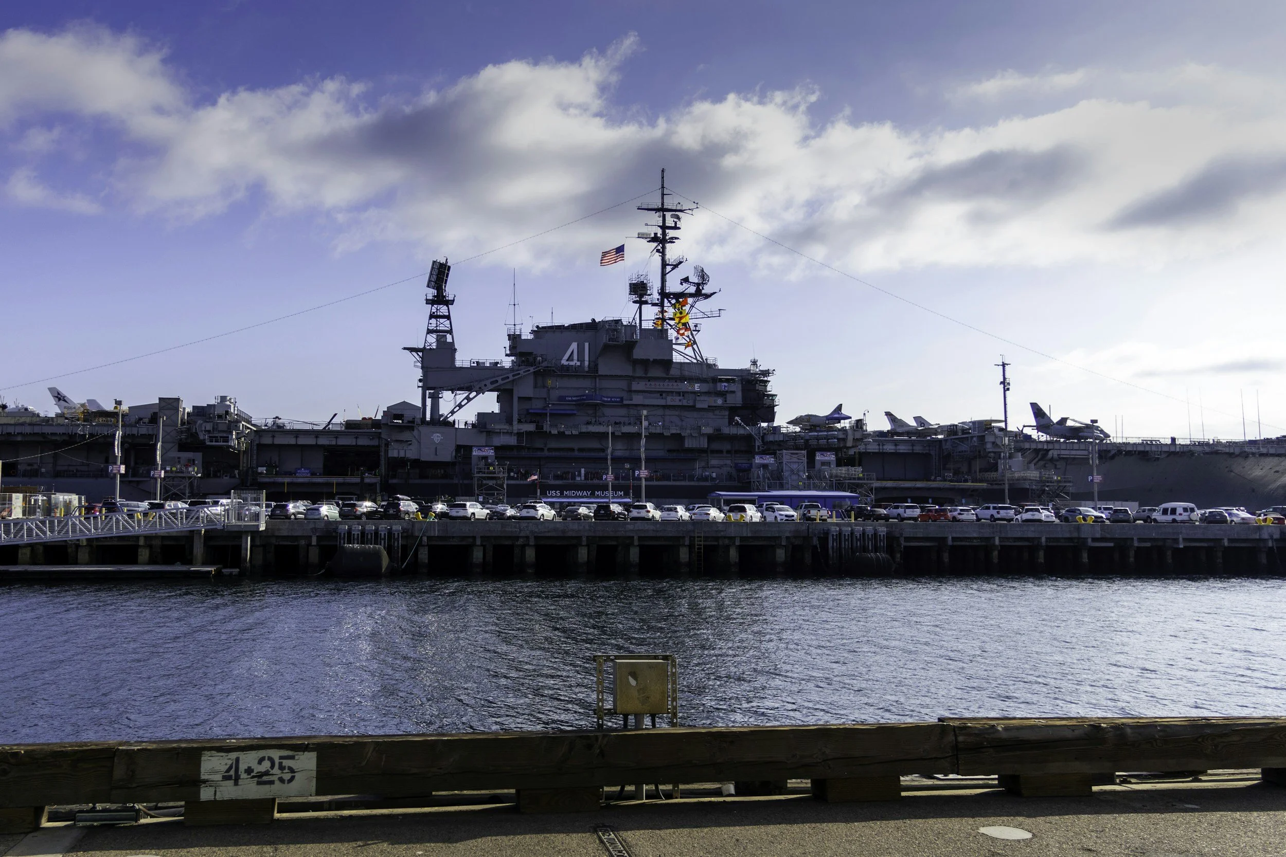 View of the USS Midway aircraft carrier with parked aircraft on deck, situated at a harbor under a cloudy sky.