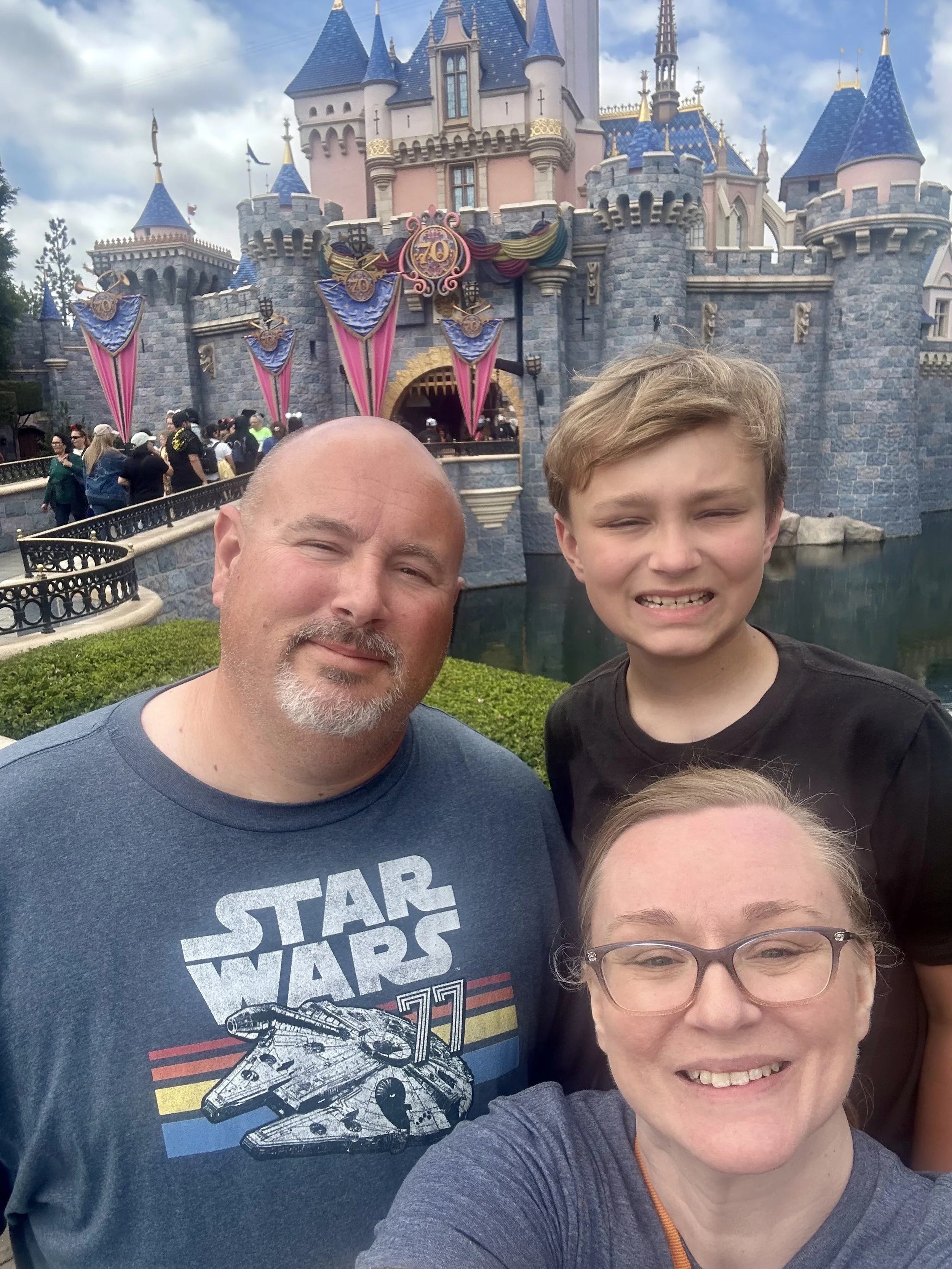 Family trip with our Star Wars T-shirts in front of Sleeping Beauty Castle at Disneyland with a cloudy sky background.