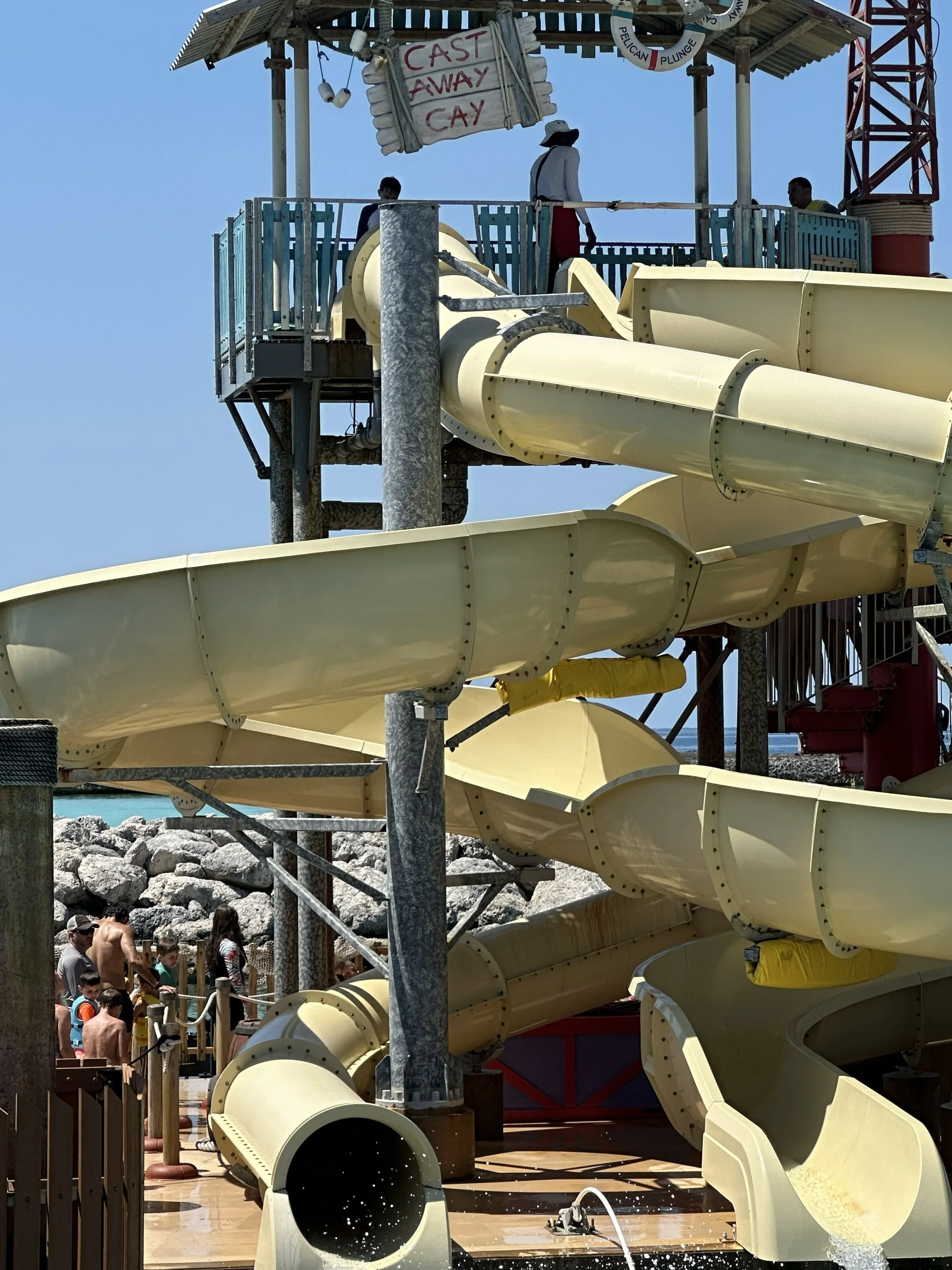 A large water slide with multiple yellow tubes and enclosed sections, part of a waterpark attraction, with people waiting in line and enjoying the slides in sunny weather.