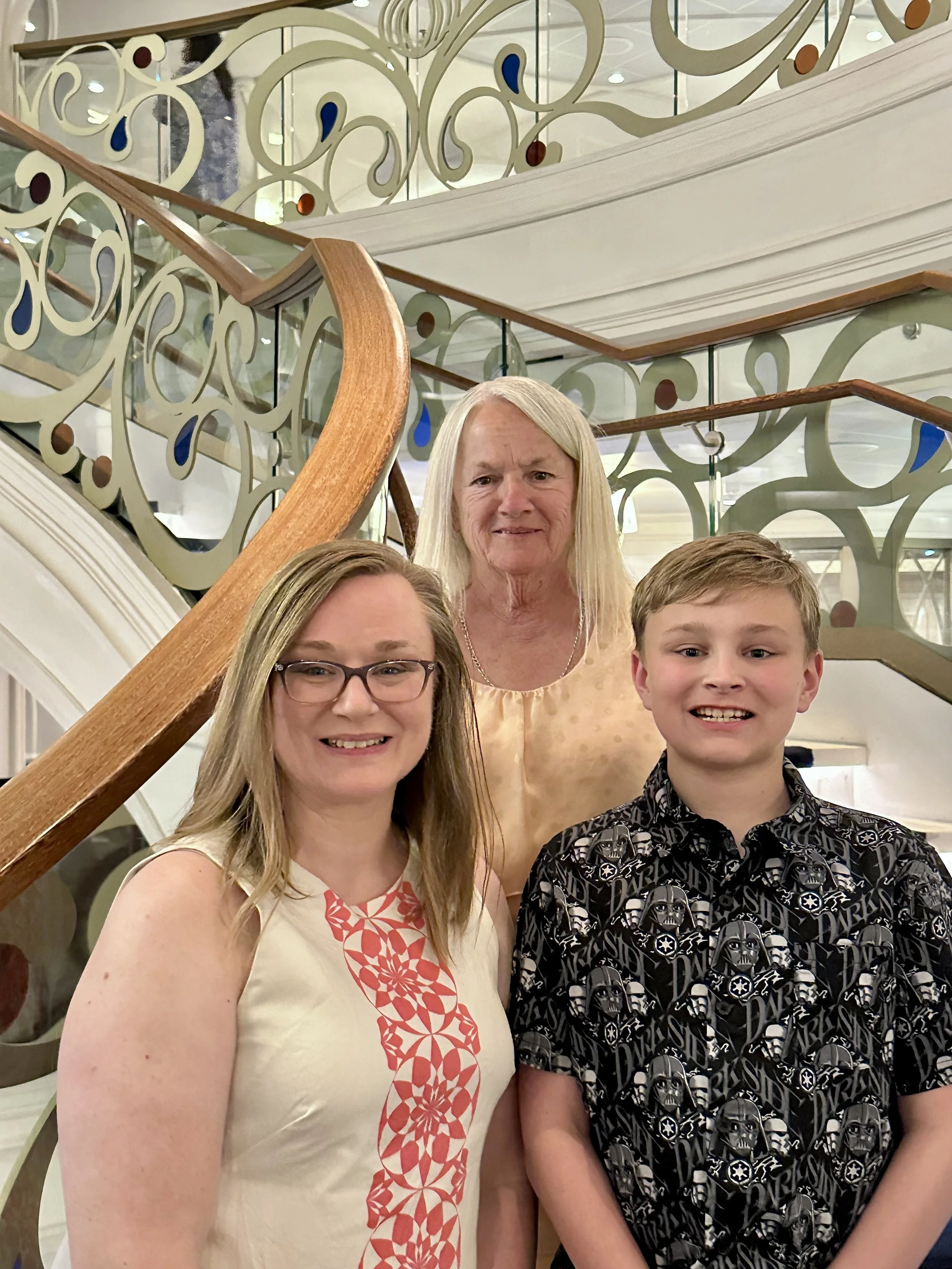 A group of four people, three women and one man, smiling for a photo inside a building with ornate decorative railings and a staircase.