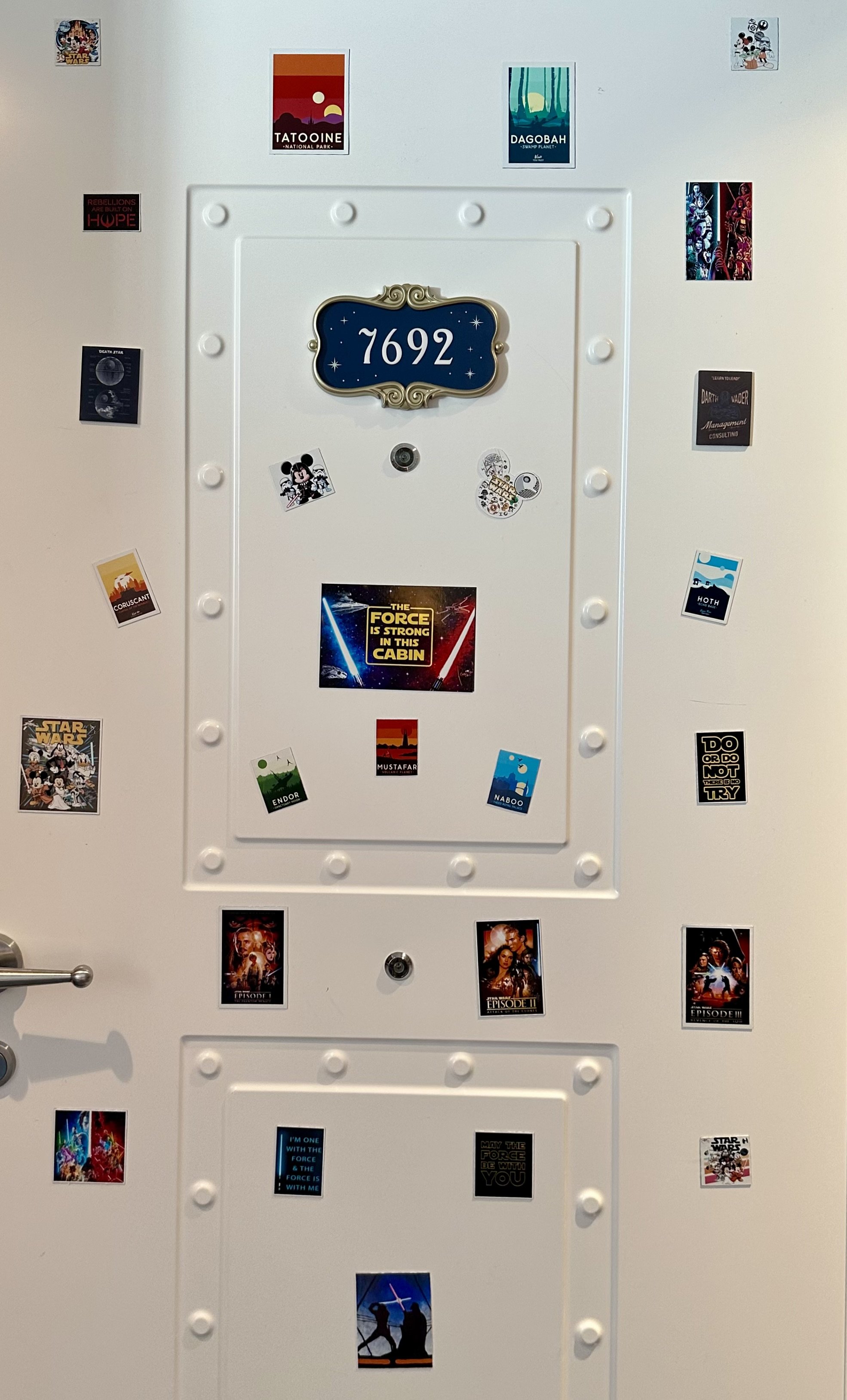 A white door with various Star Wars themed stickers and posters, including characters, planets, quotes, and symbols from the Star Wars franchise, along with a blue sign in the center displaying the number 7692.