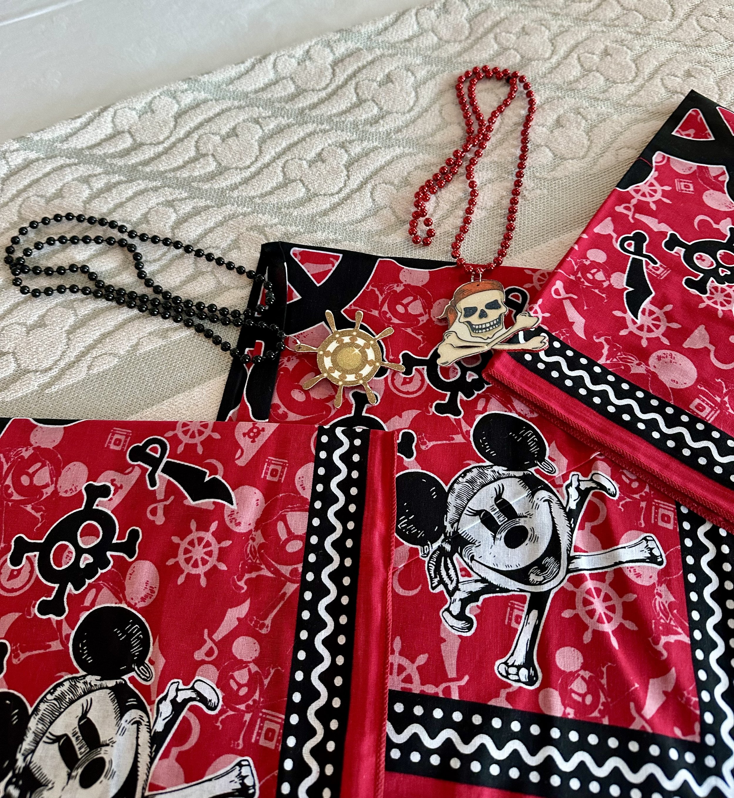 Assorted necklaces and jewelry on a decorated pink and black pirate-themed fabric, with a textured white fabric background.