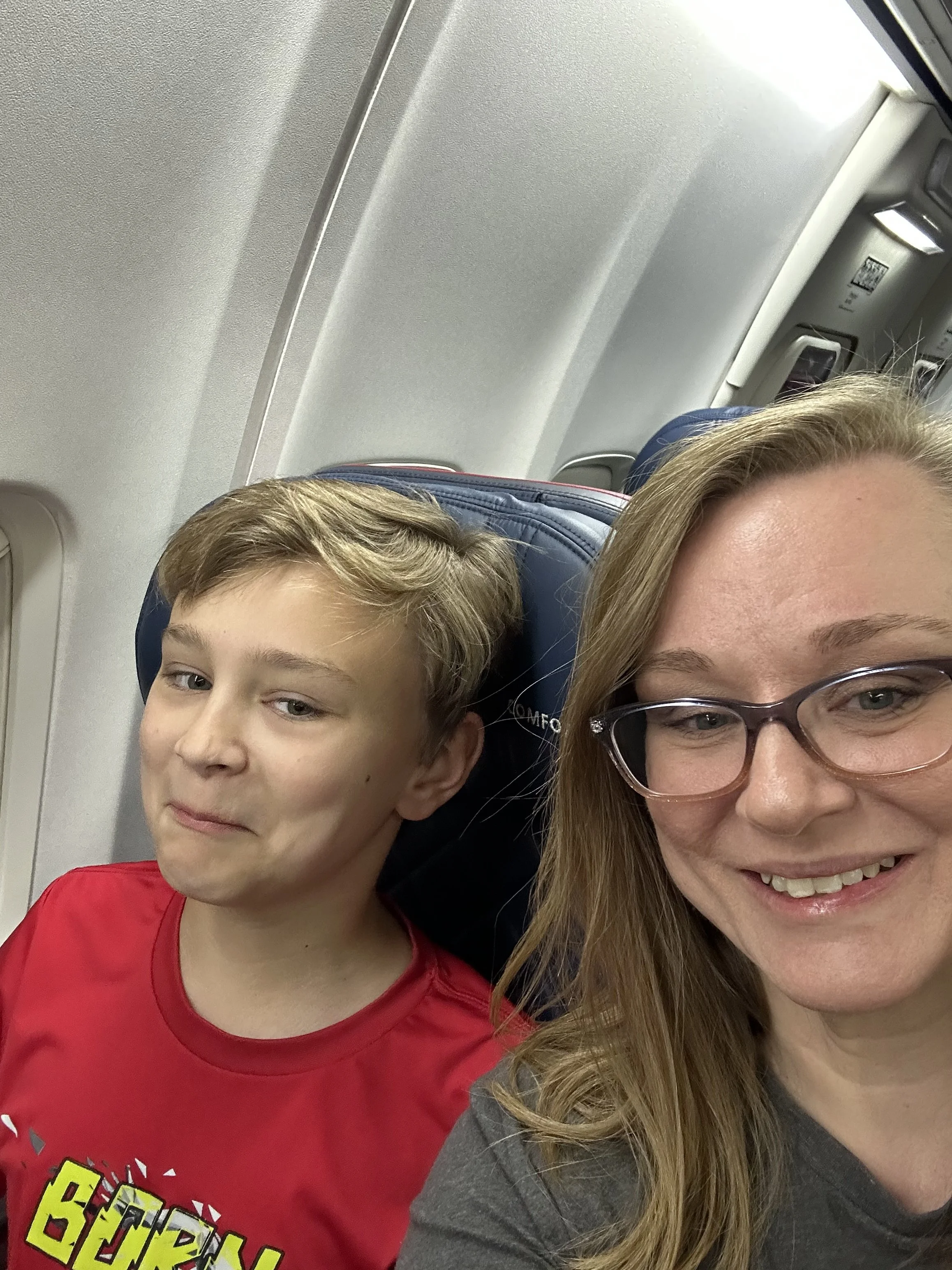 A woman with glasses and a young boy sitting next to each other on an airplane.