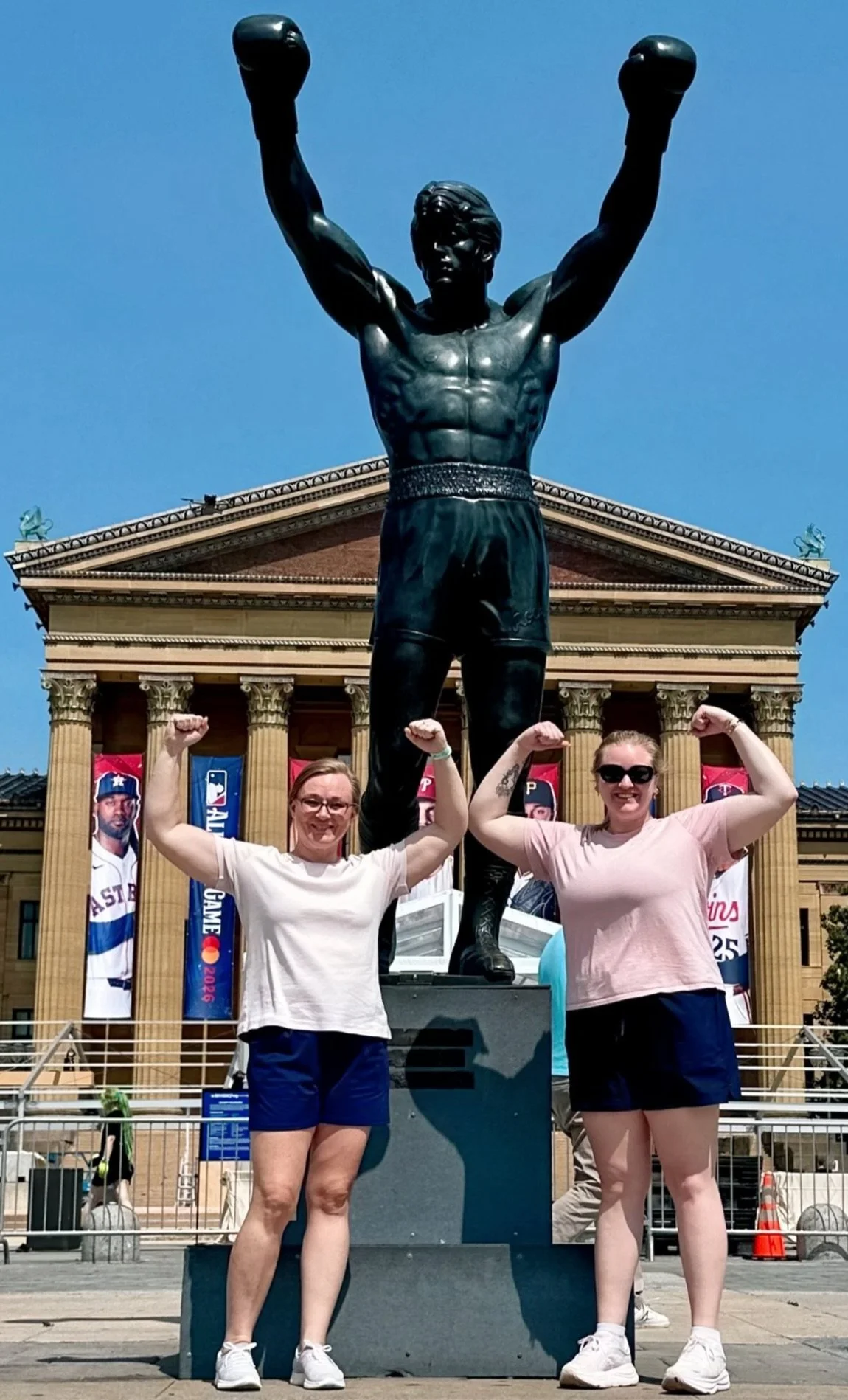 Together Travel standing in front of the Rocky statue outside the Philadelphia Museum of Art, flexing their arms and smiling on a sunny day.