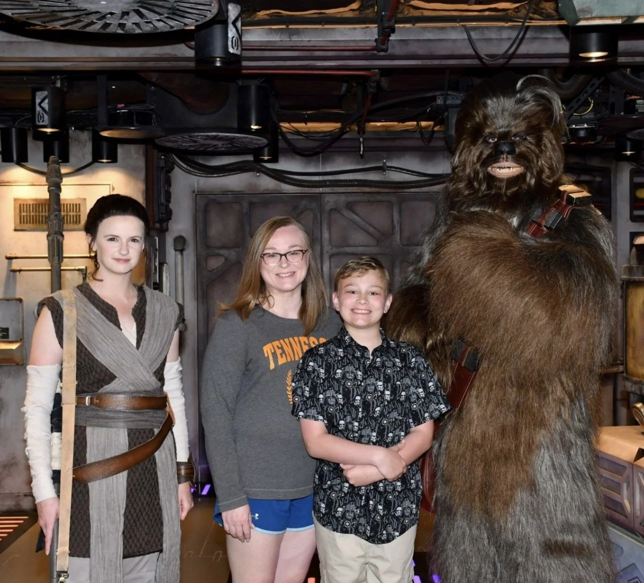 Four people, three children and one adult, standing for a photo with a large Chewbacca character from Star Wars in a sci-fi themed setting.