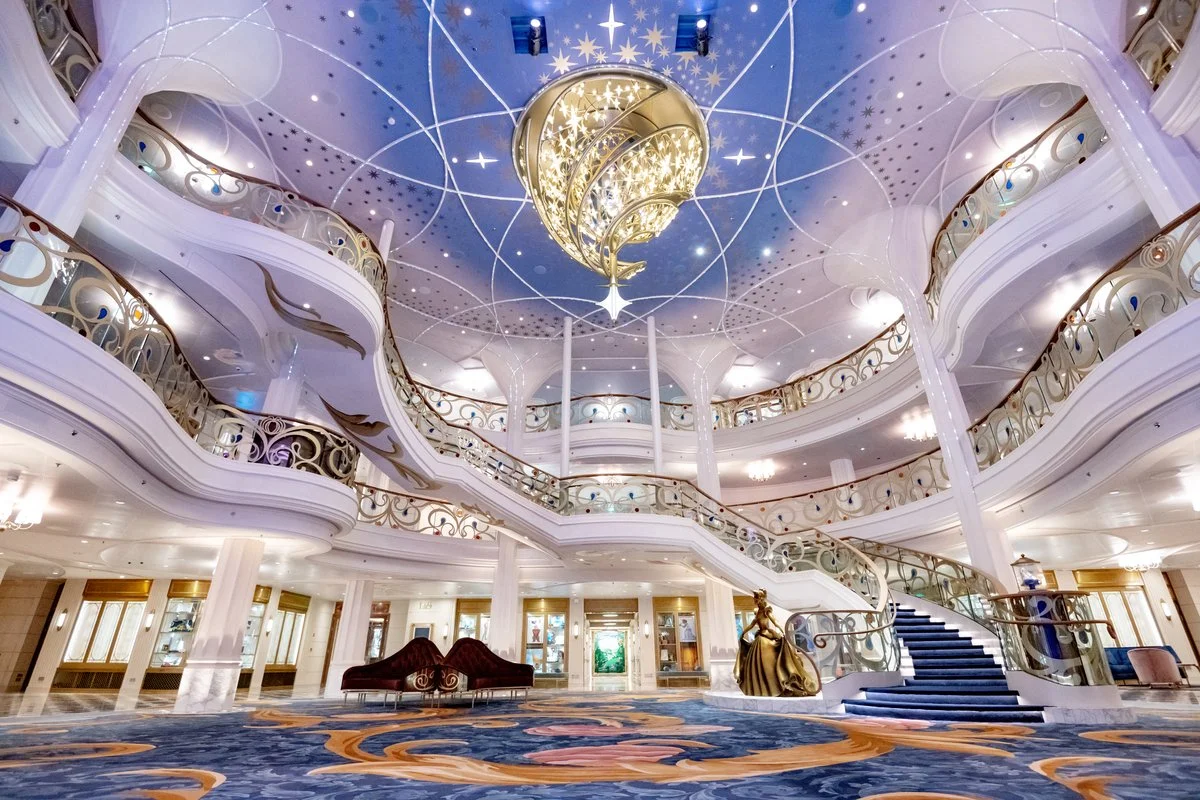 Elegant hotel lobby with a grand staircase, ornate gold railings, and a large chandelier hanging from a decorated ceiling.