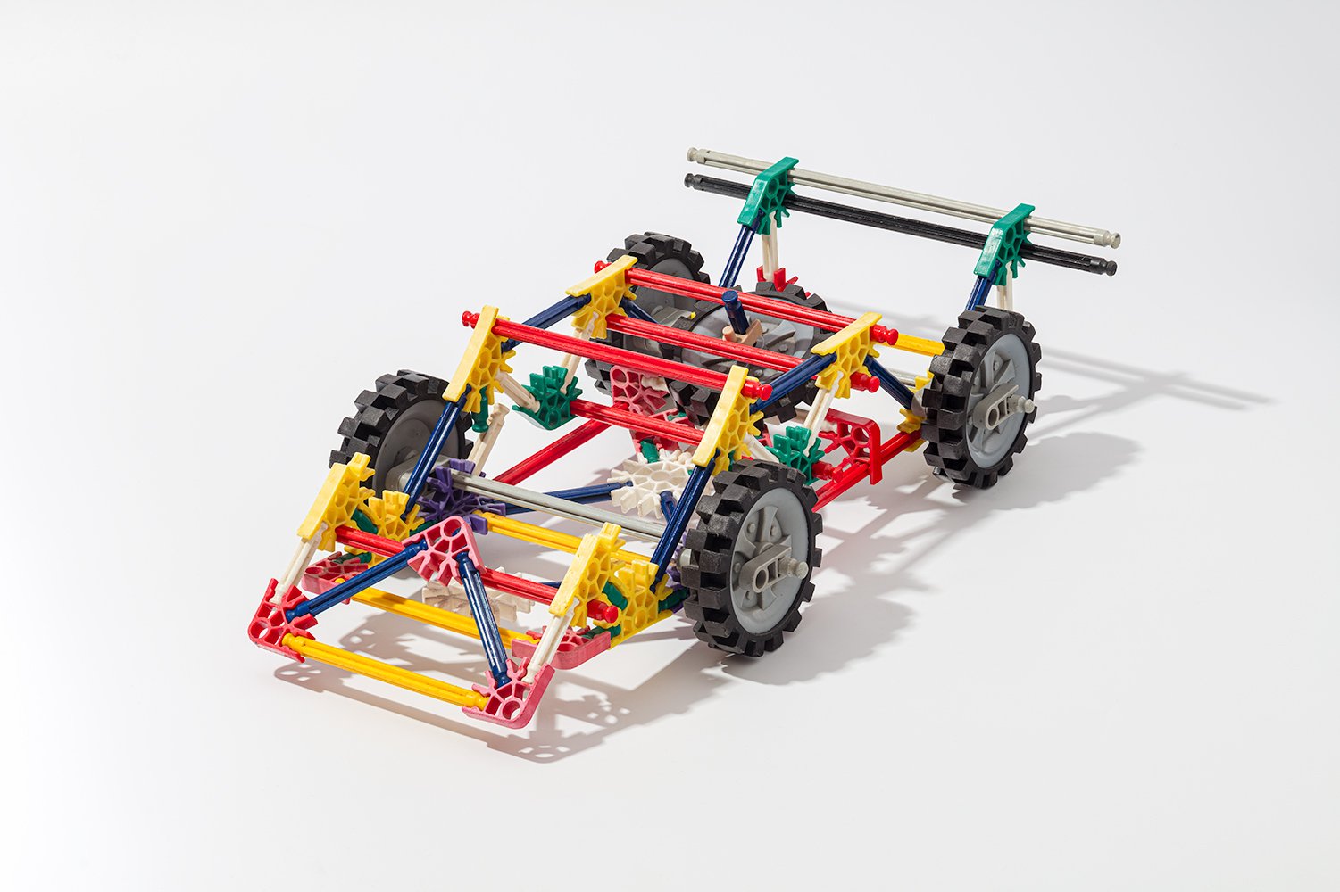 K’NEX construction toy vehicle with wheels, red, yellow, green, blue, and gray plastic parts on white background.