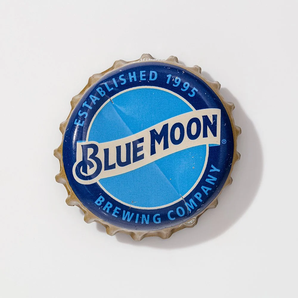 A bottle cap from Blue Moon Brewing Company featuring a blue and white label with the company's name and establishment year, 1995.
