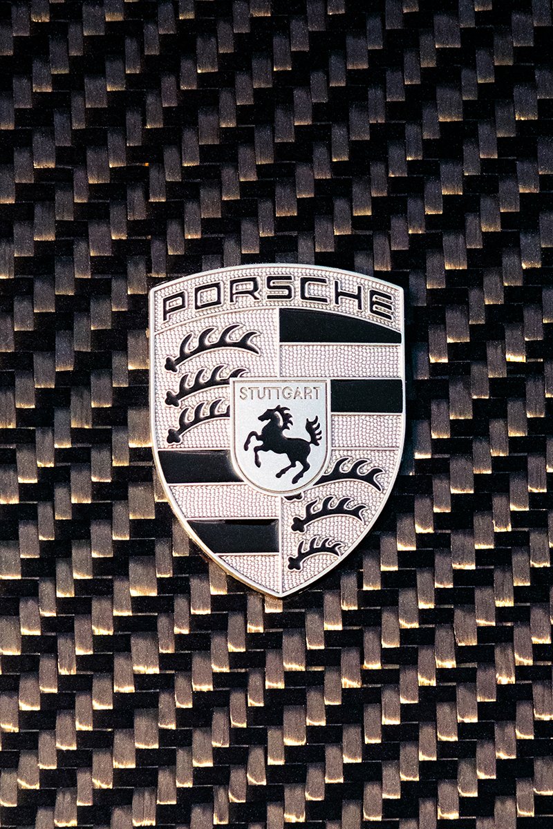 Close-up of a Porsche emblem on a carbon fiber background.