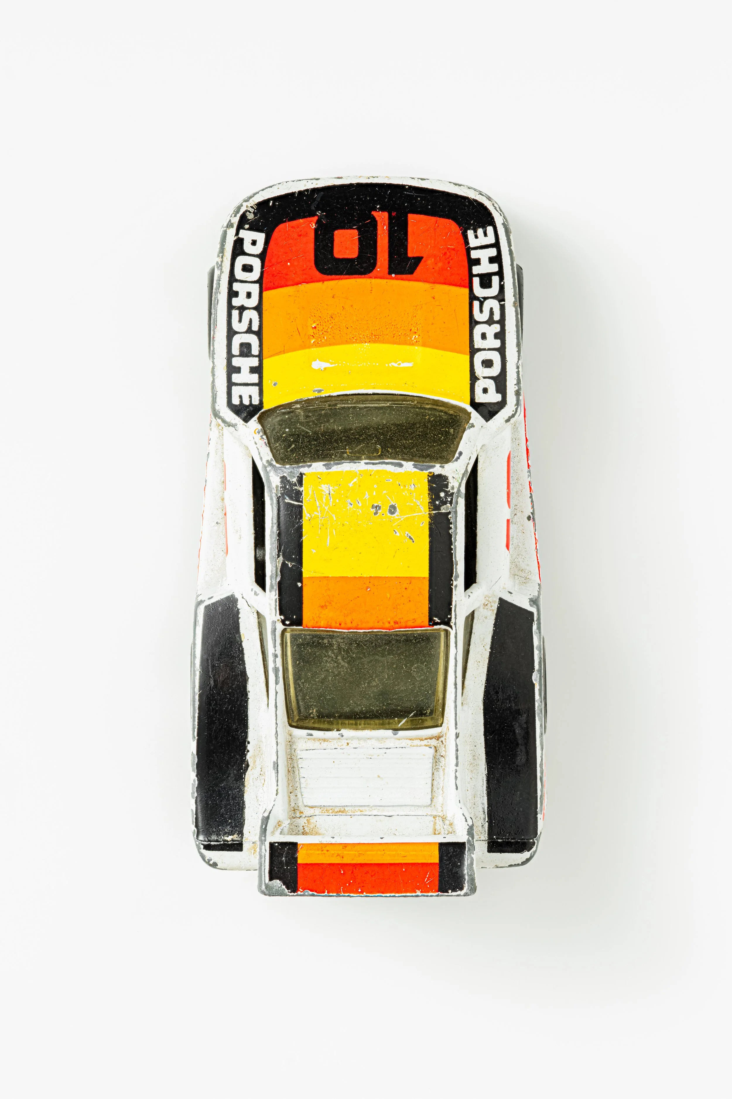 Top view of a weathered white toy car with orange and yellow stripe markings on the hood and rear, against a white background.