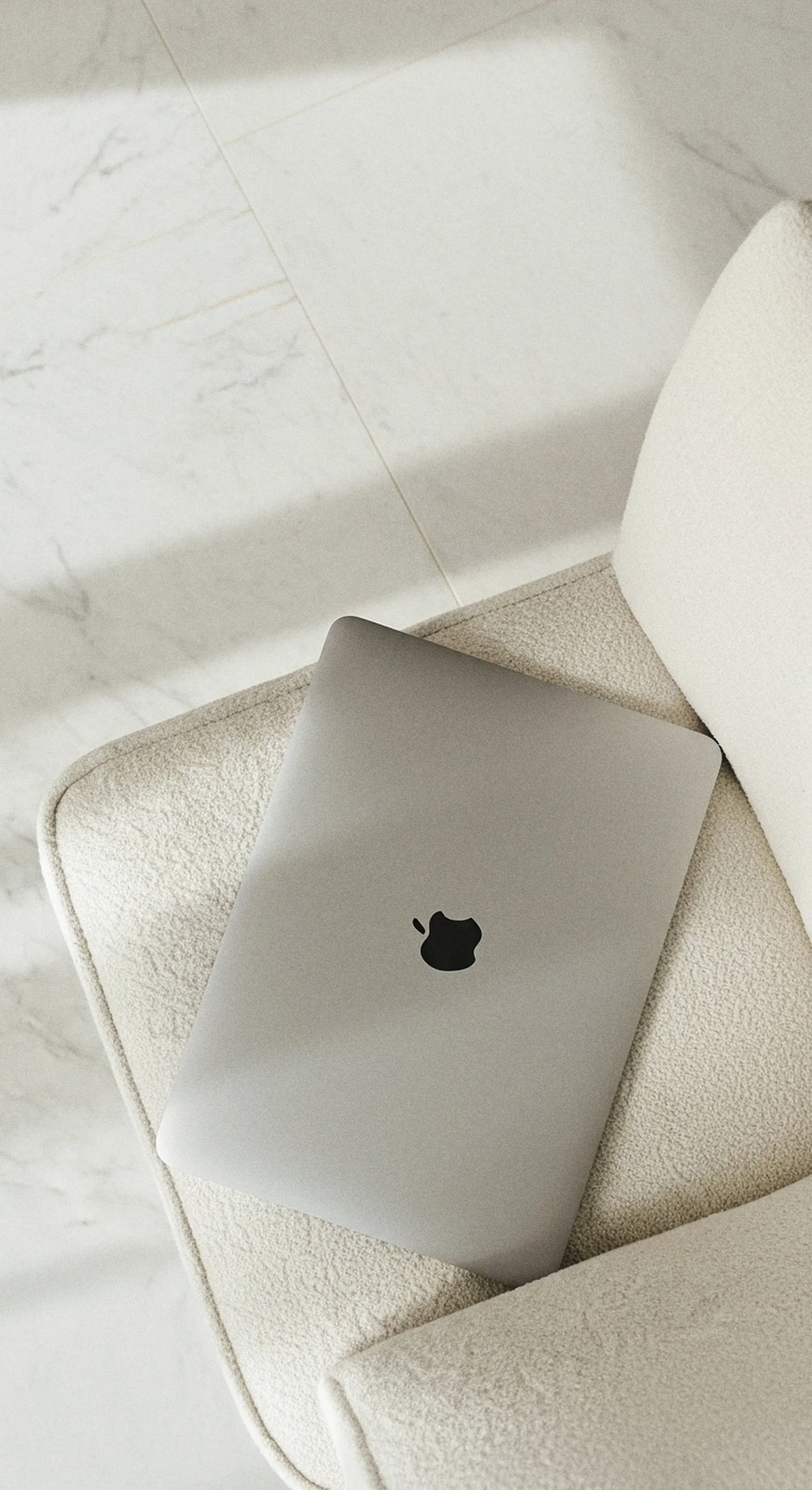 A closed silver MacBook laptop with an Apple logo on the top, resting on a cream-colored textured chair.