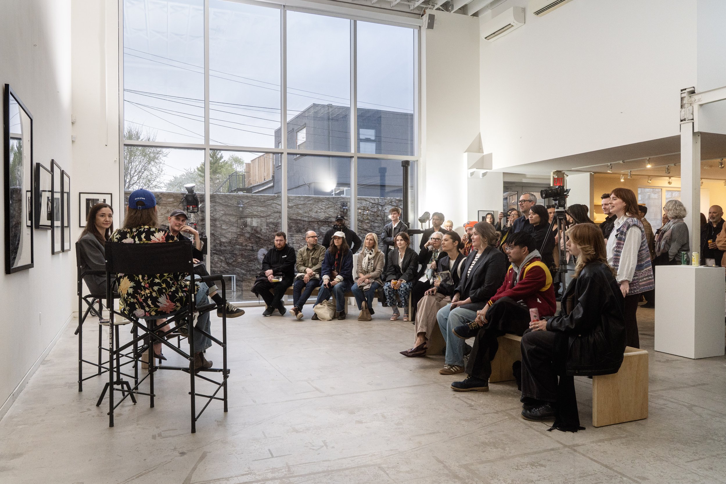 Audience watch a live panel interview with photographers for the opening night of gallery exhibition featuring black and white photography.