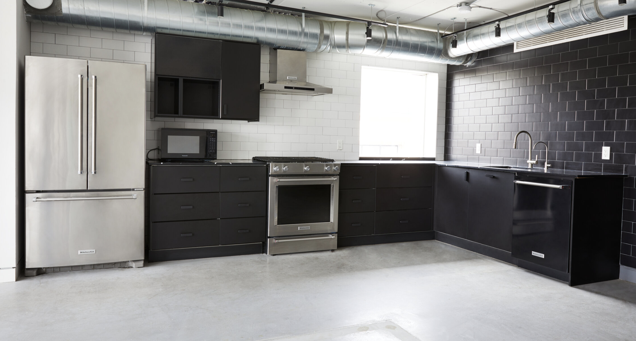 Bright, comfortable studio space with stainless steel kitchen appliances, stove and oven, range hood, refrigerator and freezer, and black counters and cupboards. Built in dishwasher with sink and east facing window
