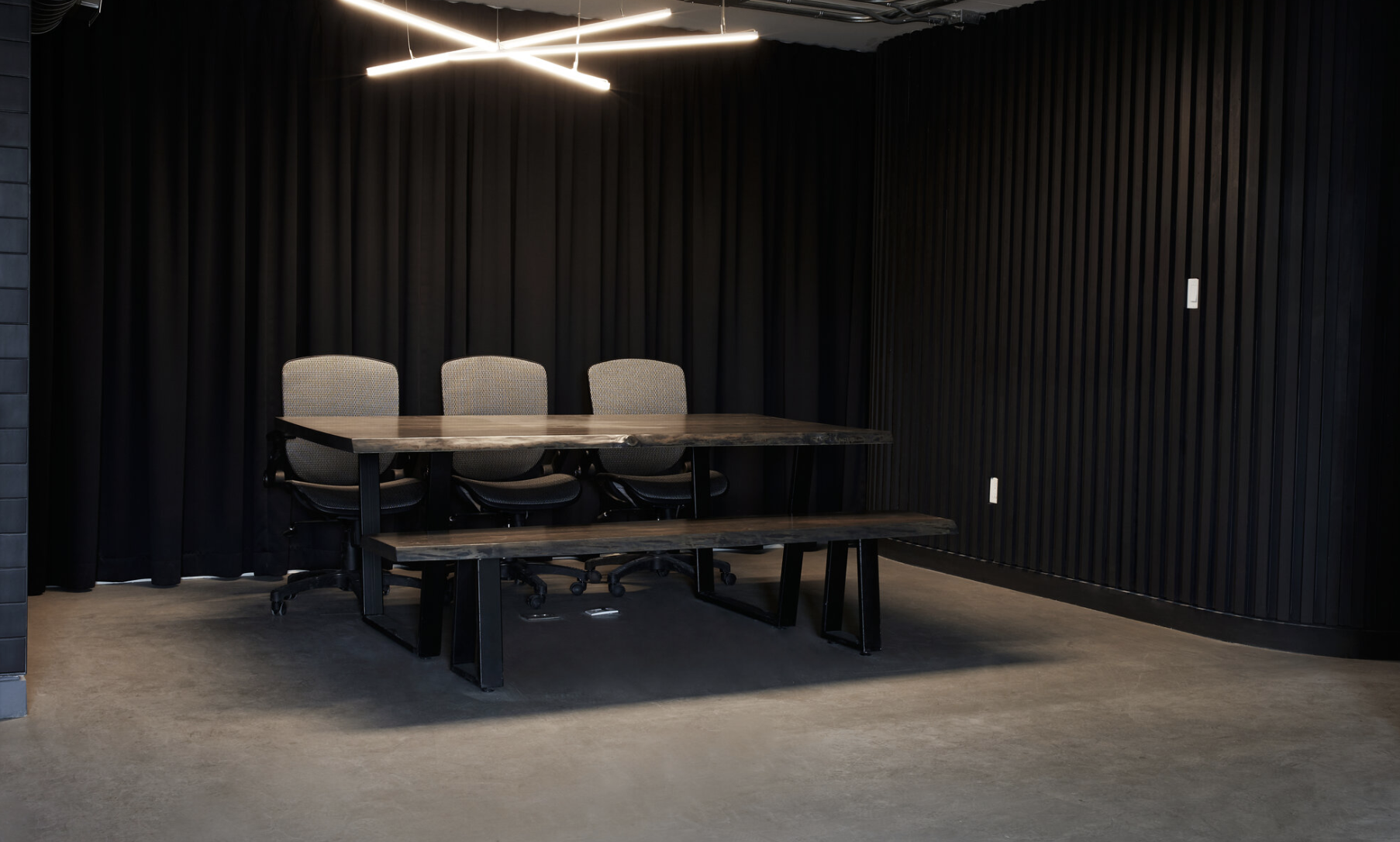 Polished dining table with cushioned office chairs, black walls, and modern ceiling light