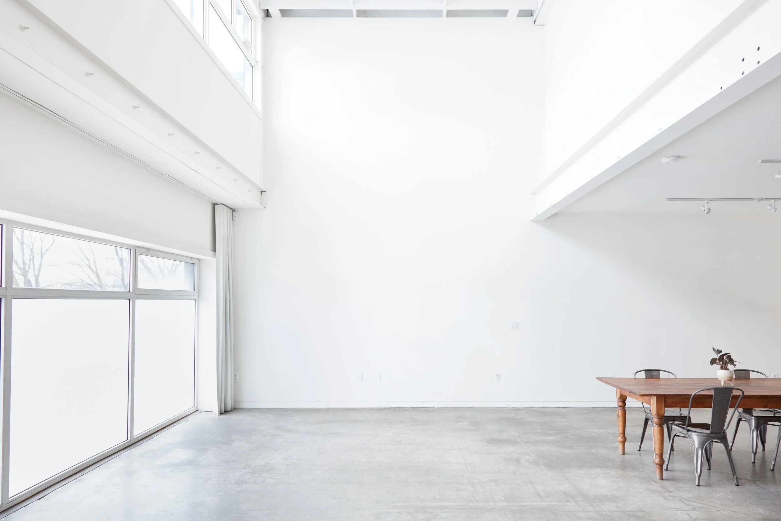 Studio space with white walls, high ceilings, south facing windows, and wooden client table