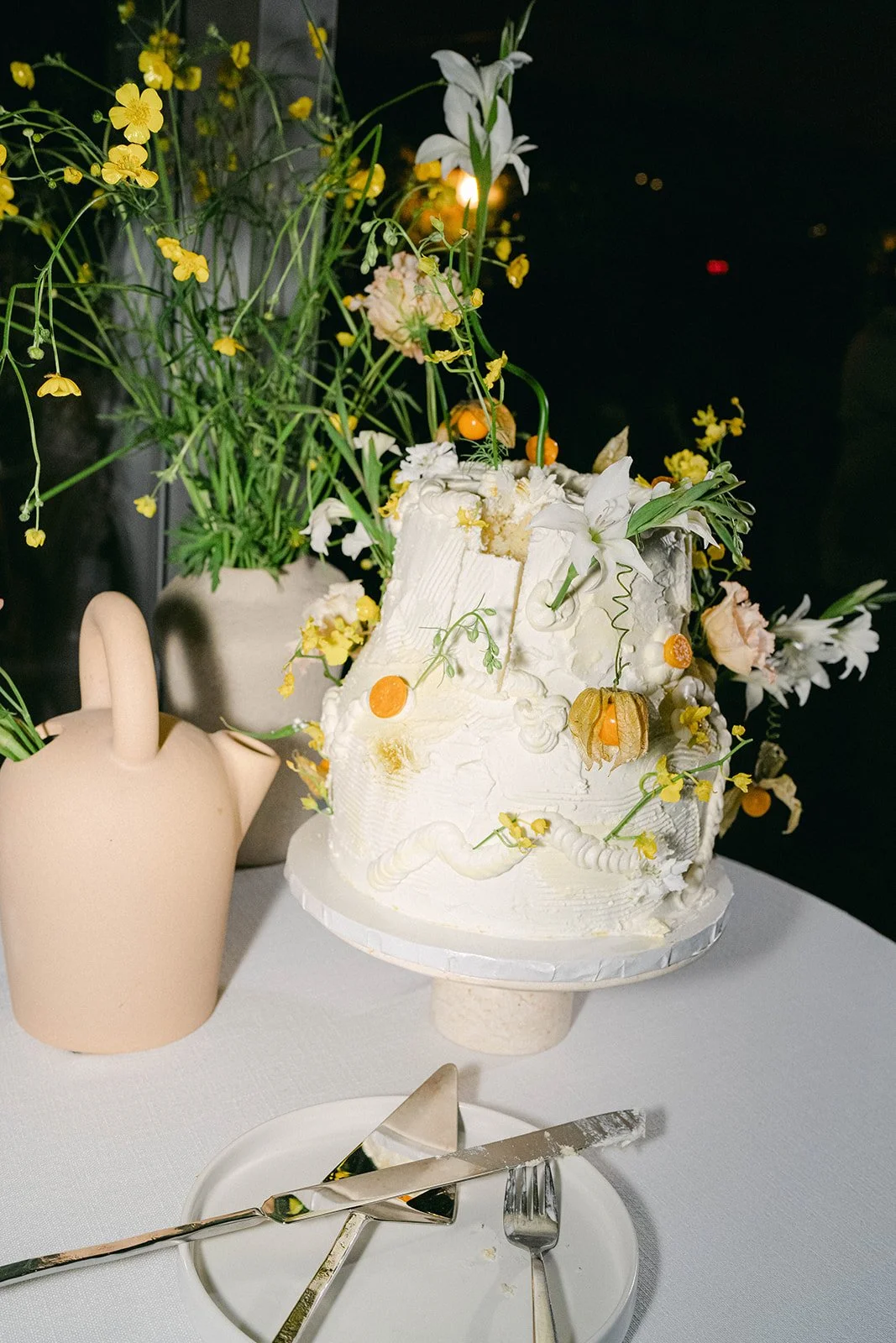 Two tier wedding cake decorated with white frosting, golden berries, and florals 
