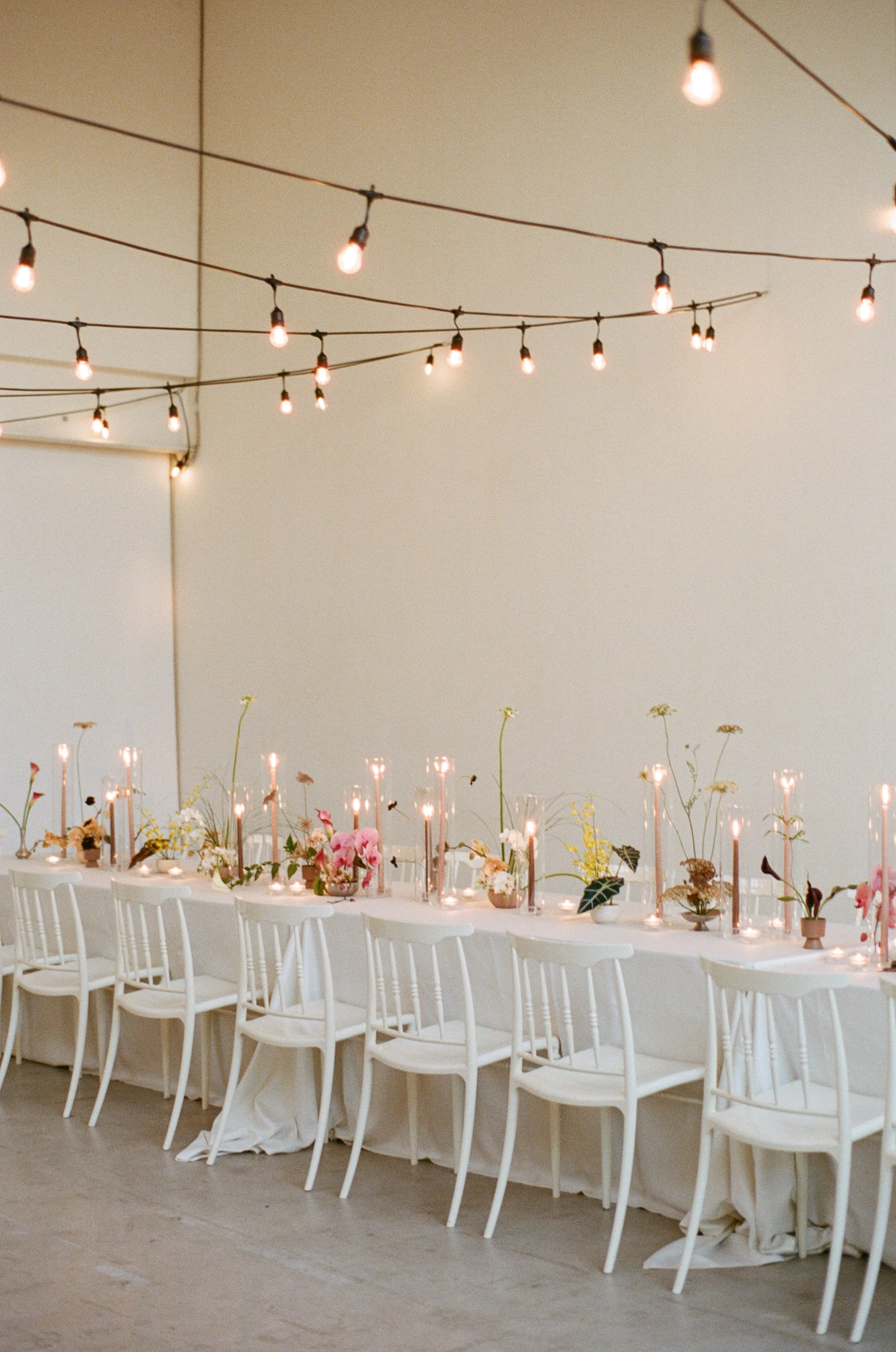 String lights hang above an elegant dinner setup for a wedding reception inside a Toronto studio space and event venue
