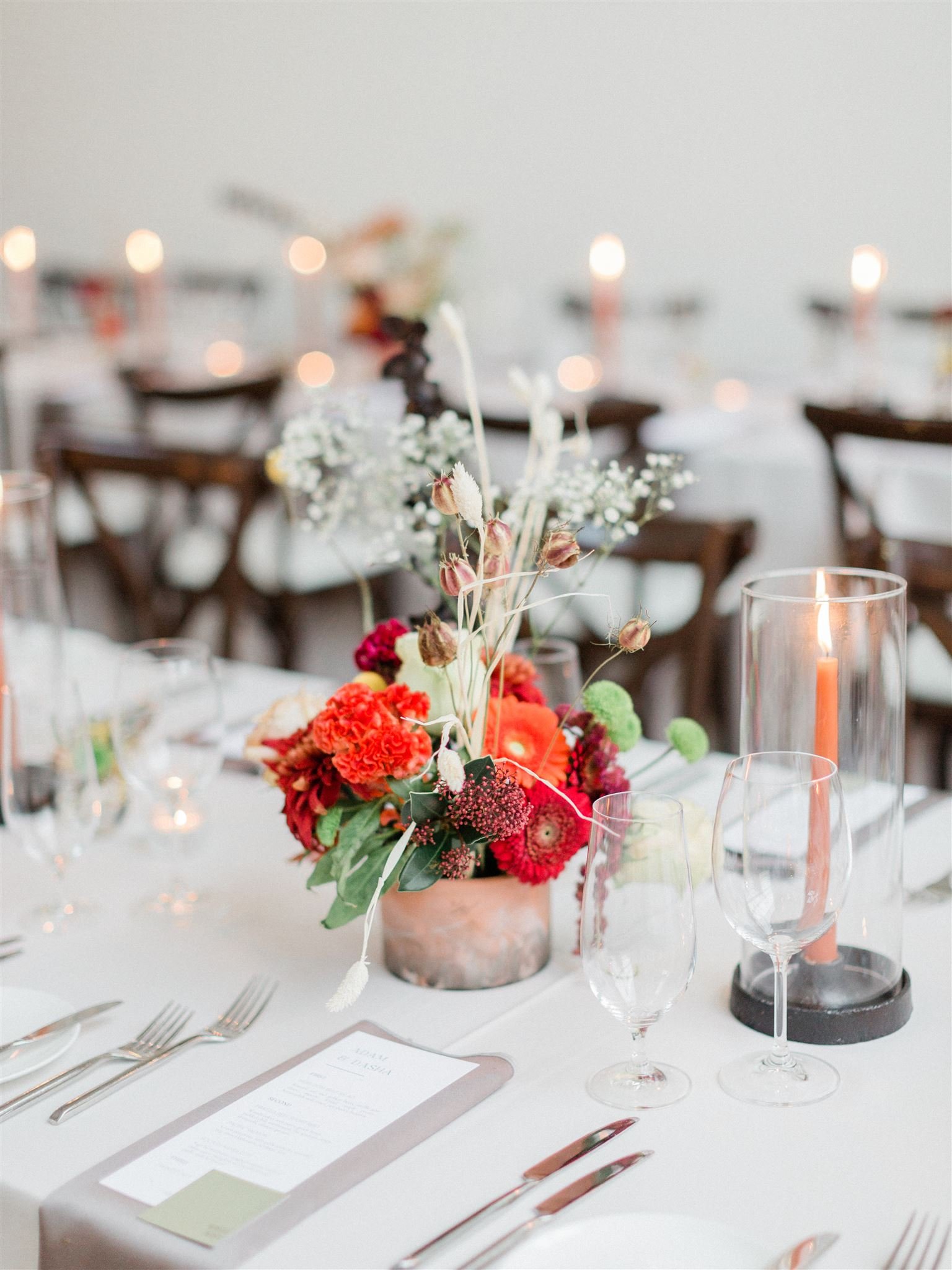 Candles and floral centrepieces displayed on a dinner table for a wedding reception. Menu place cards and utensils are also on the table 
