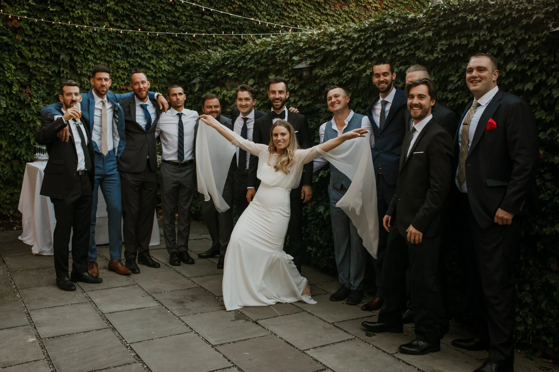 Bride poses in front of the groom and groomsmen while they're outside on the private patio of a Toronto wedding venue and studio space