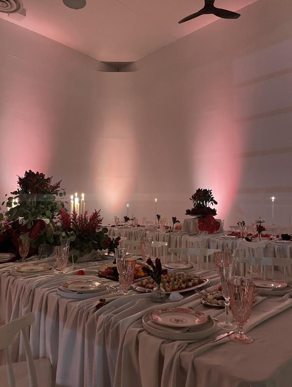 Light pink and red floor lights light up a cyclorama wall inside a Toronto studio rental space and event venue. Tables are decorated with layered linen, candles, fresh flowers, food, and tableware.