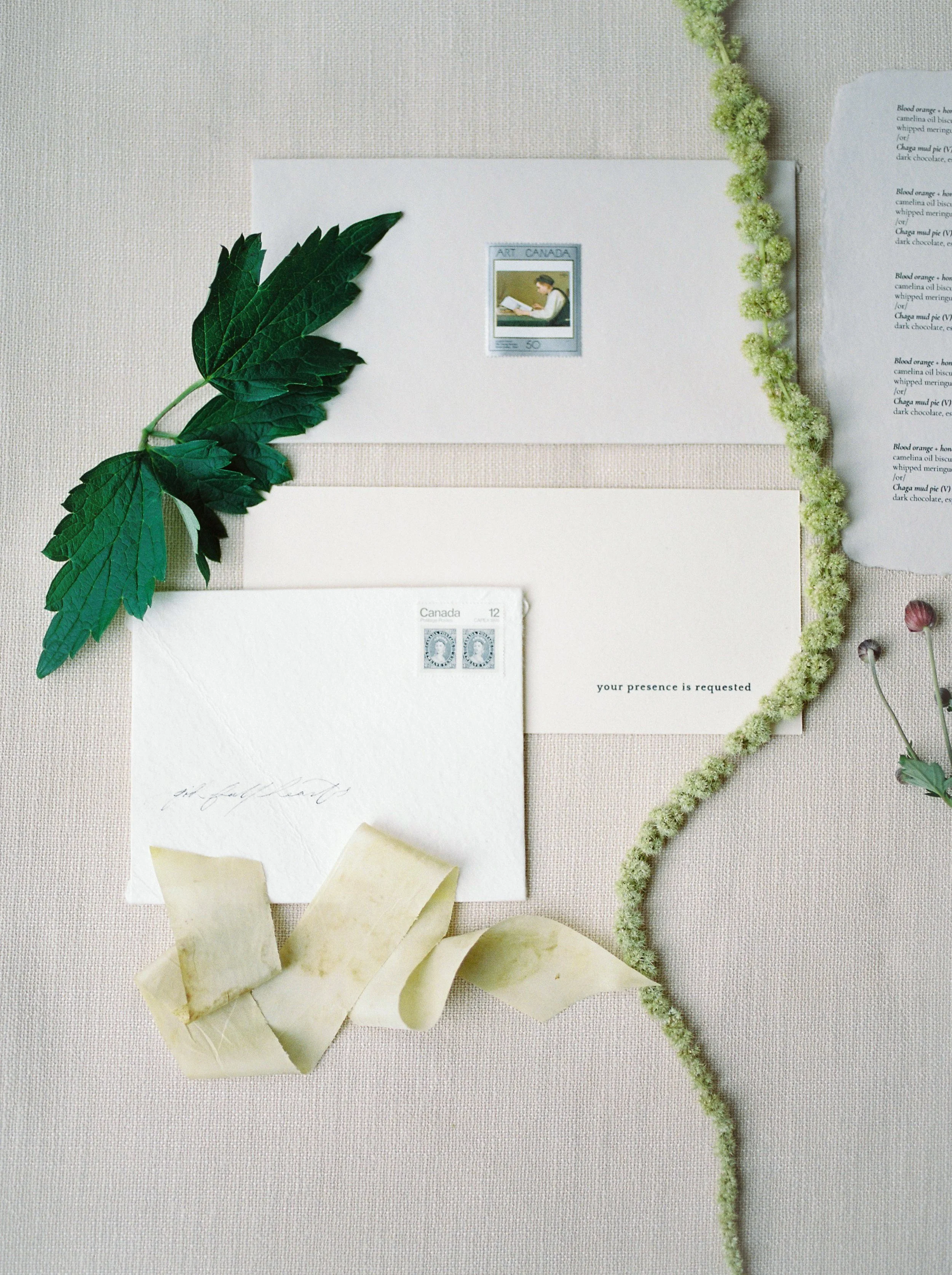 An envelope reads “your presence is requested” and is surrounded by delicate florals and greenery.