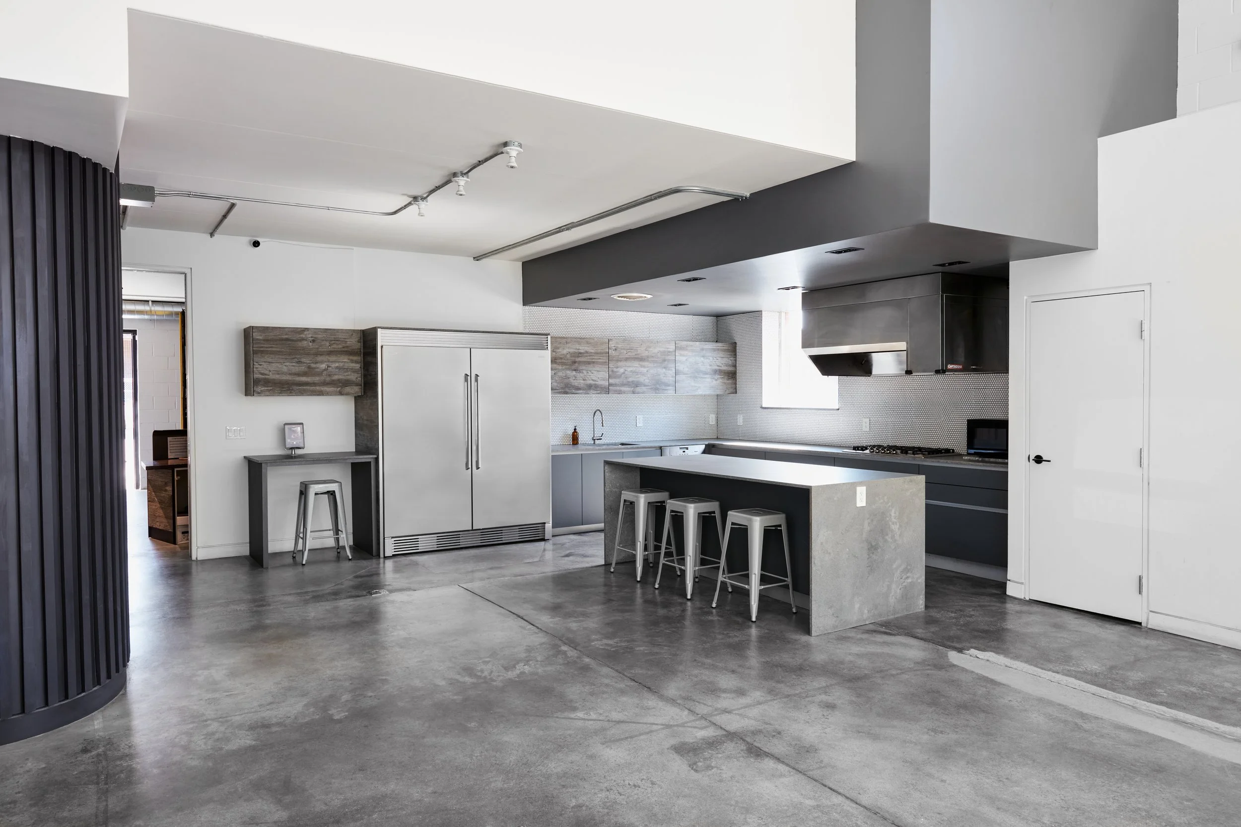 Modern full kitchen island, bar stools, stove range, large refrigerator and freezer, built in dishwasher, cupboards, and countertops.