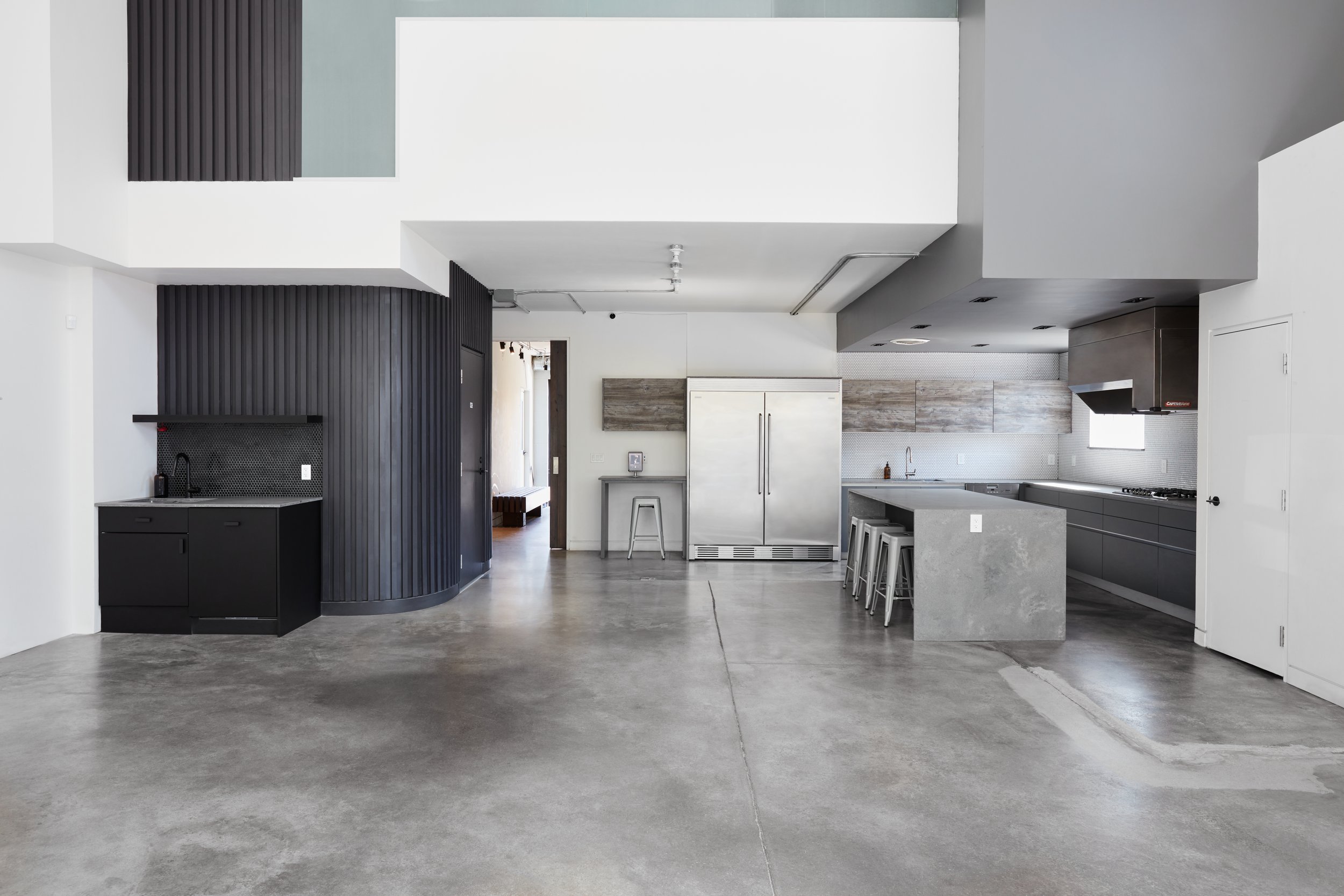Modern full kitchen island, bar stools, stove range, large refrigerator and freezer, built in dishwasher, cupboards, and countertops. There's a kitchenette with a built in dishwasher and sink.