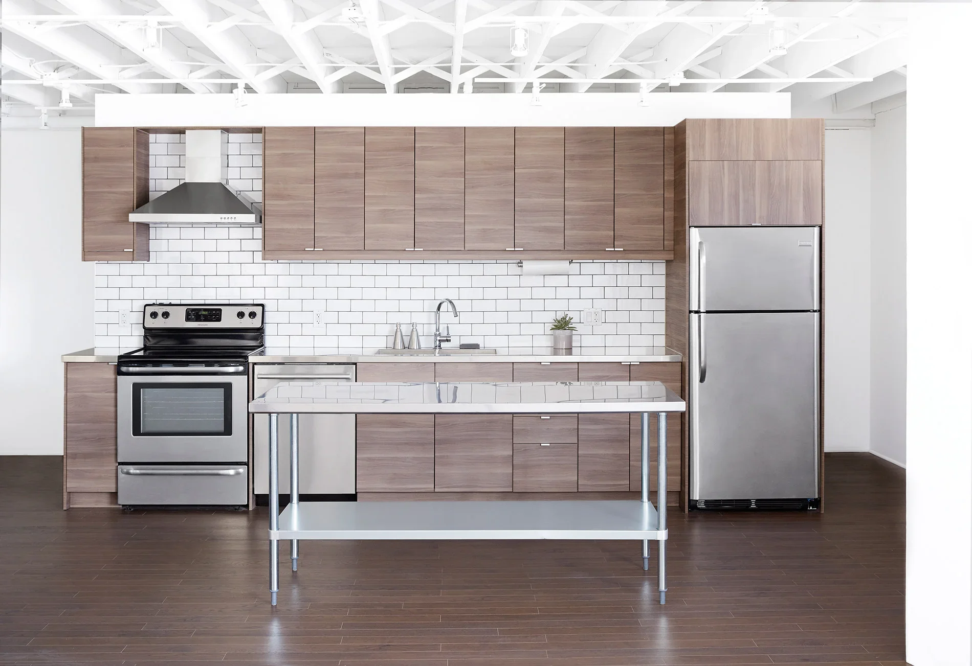 Full kitchen featuring a stainless steel island, refrigerator and freezer, oven with stovetop, built in dishwasher, and cupboards. Hardwood floors.