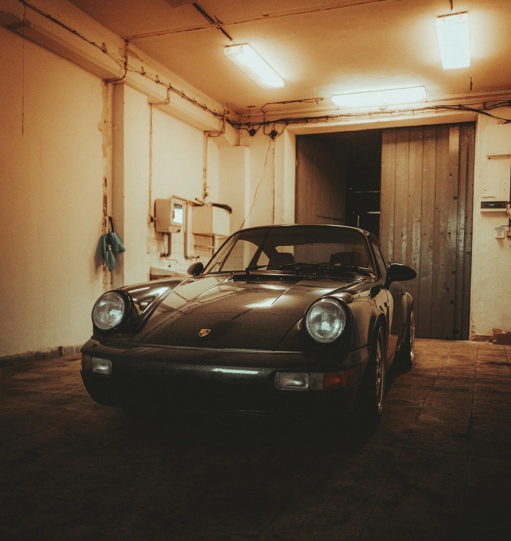 A black vintage Porsche sports car parked inside a dimly lit garage with a wooden door in the background.