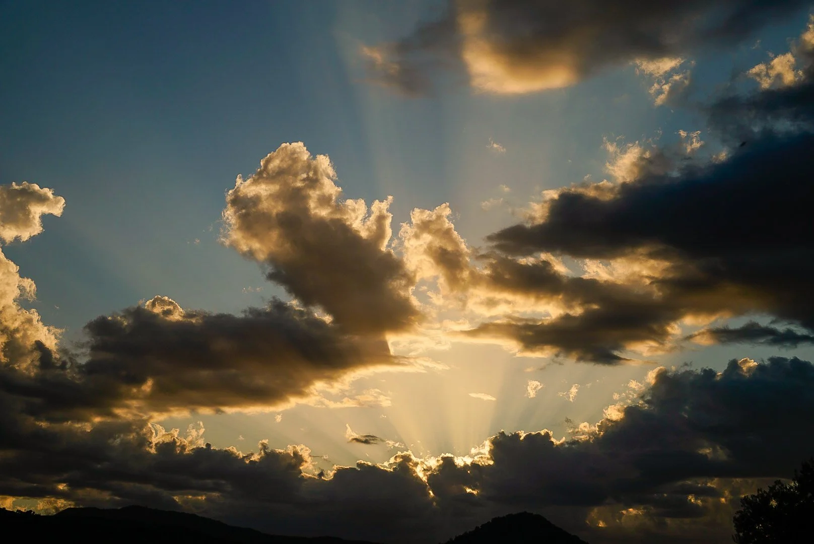 Sonnenstrahlen brechen durch Wolken über einer bergigen Landschaft bei Sonnenuntergang.