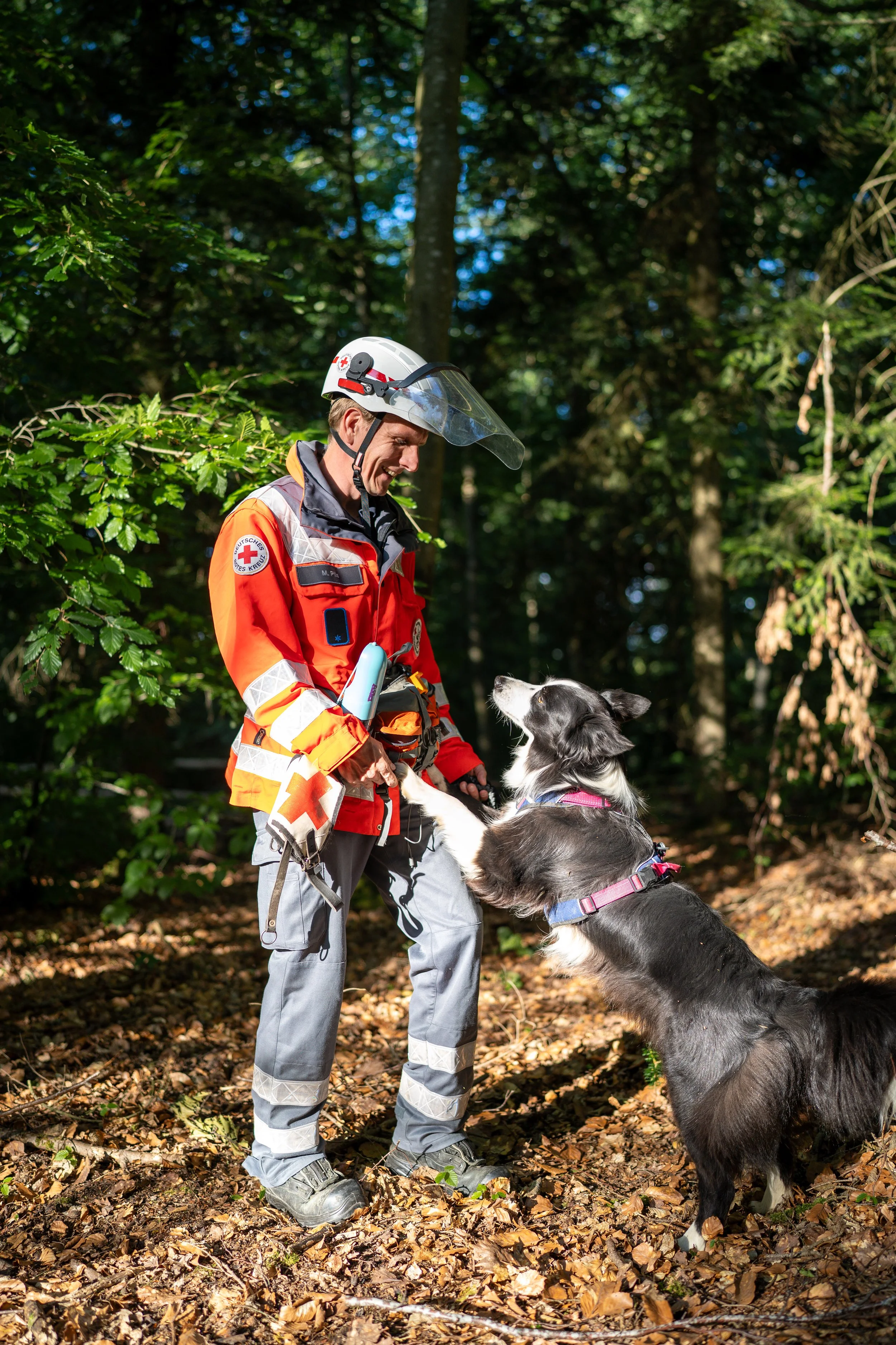 Ein Mann in einem Rettungsdienst-Uniform speist einen Hund im Wald.