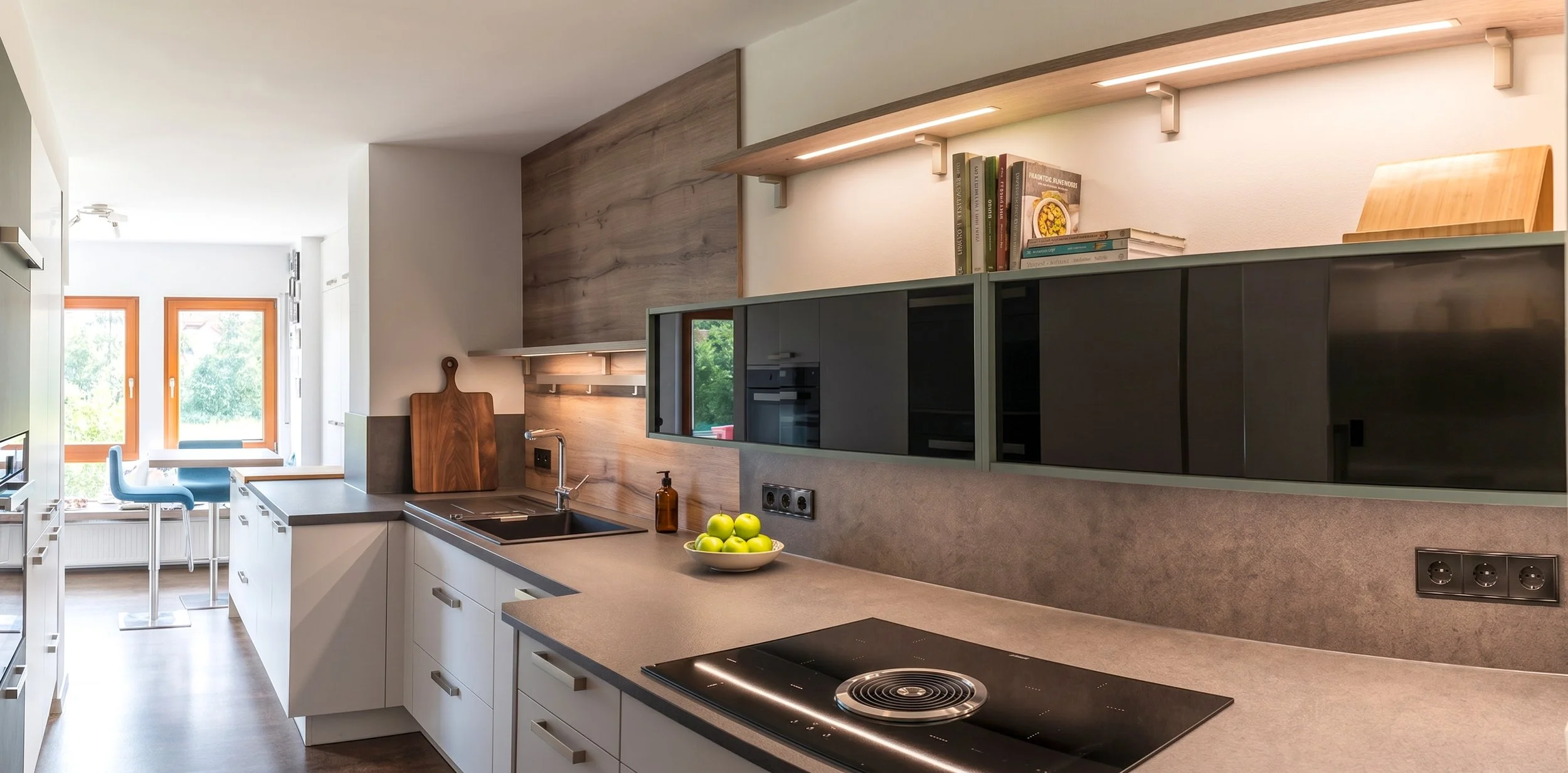 Moderne Küche mit weißen Schränken, dunklem Herd, Frühstückstheke, und Blick auf einen Balkon mit Teelicht.