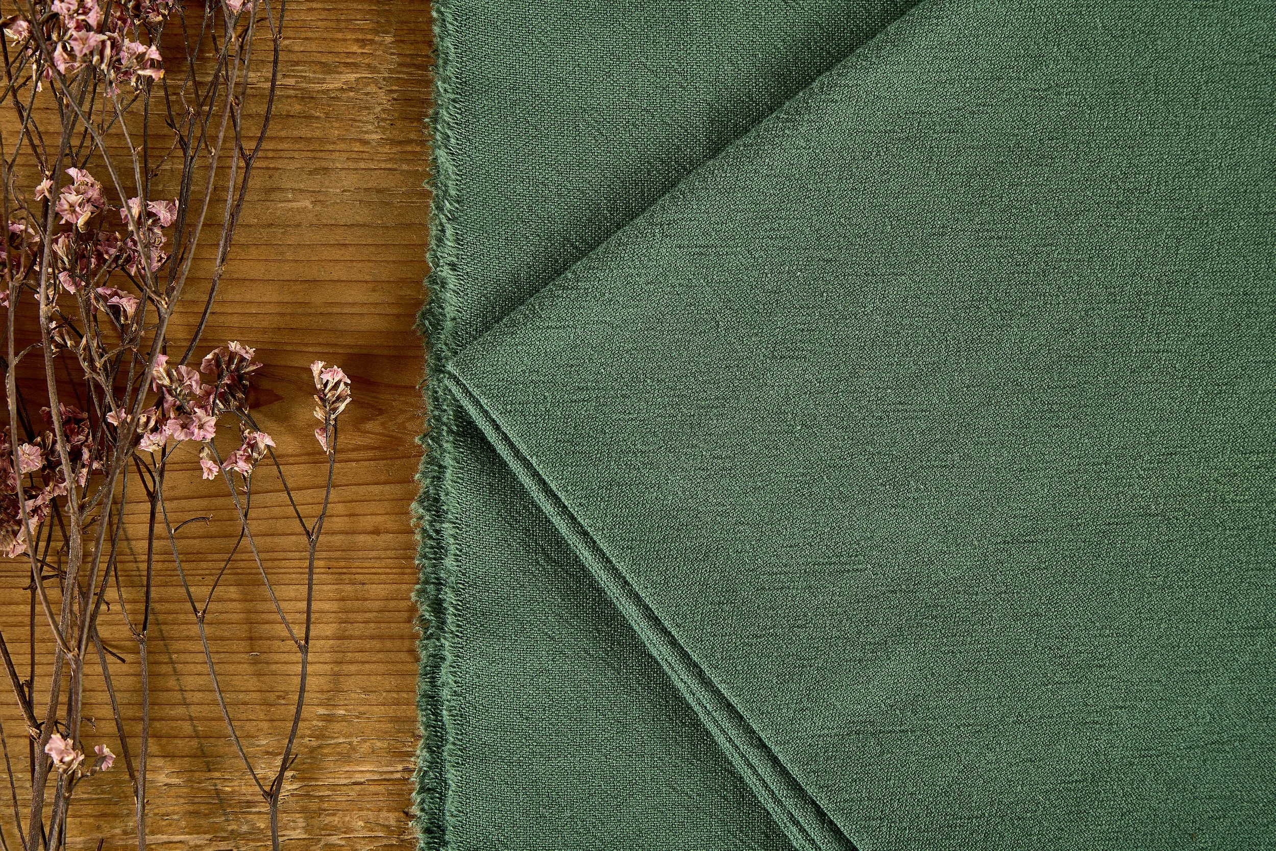 Forest green 30 linen 70 cotton plain woven fabric folded flat on rustic wooden board with selvage fringe details