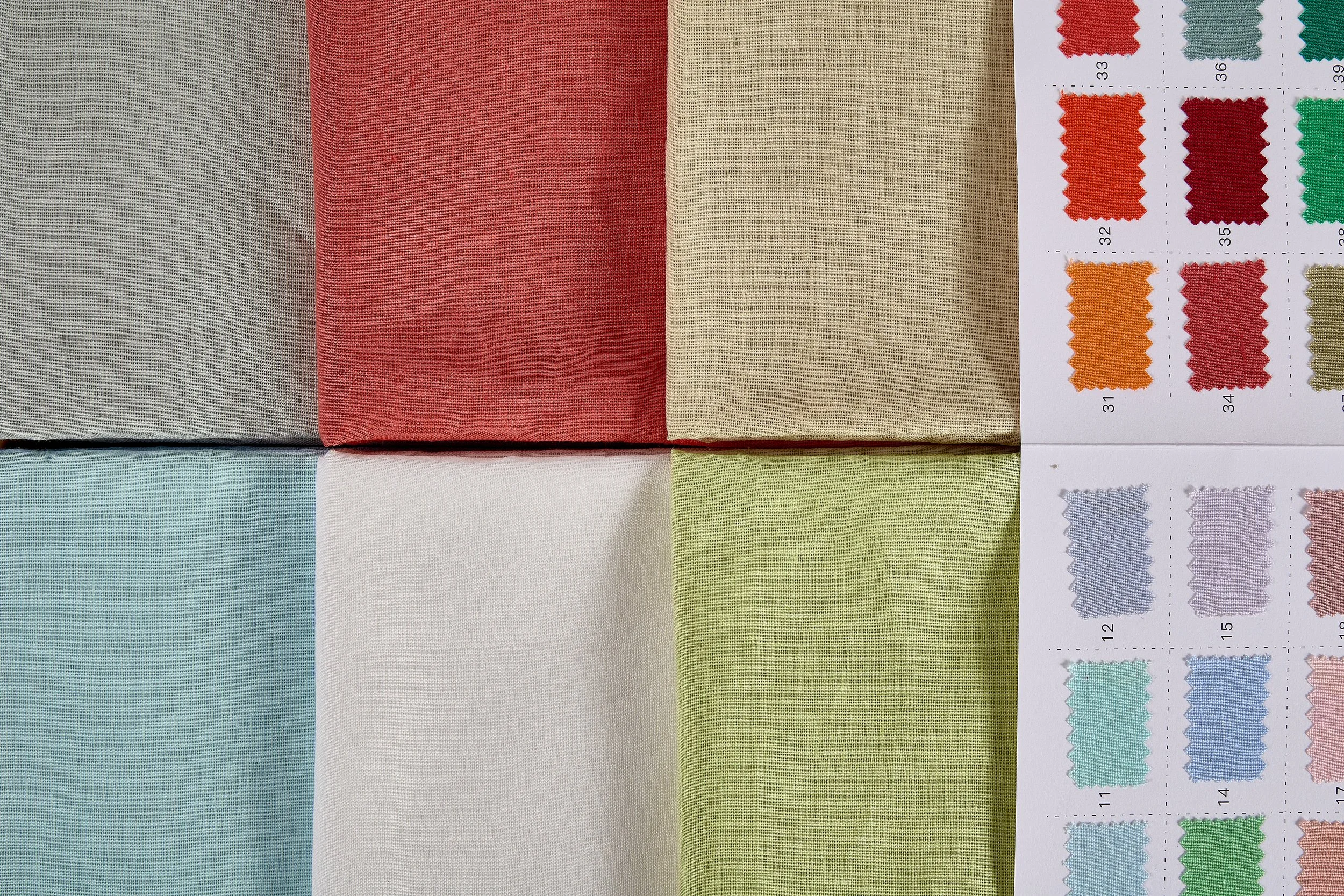 Folded 55% linen 45% cotton fabric assortment displayed alongside an official color swatch book for wholesale textile sampling.