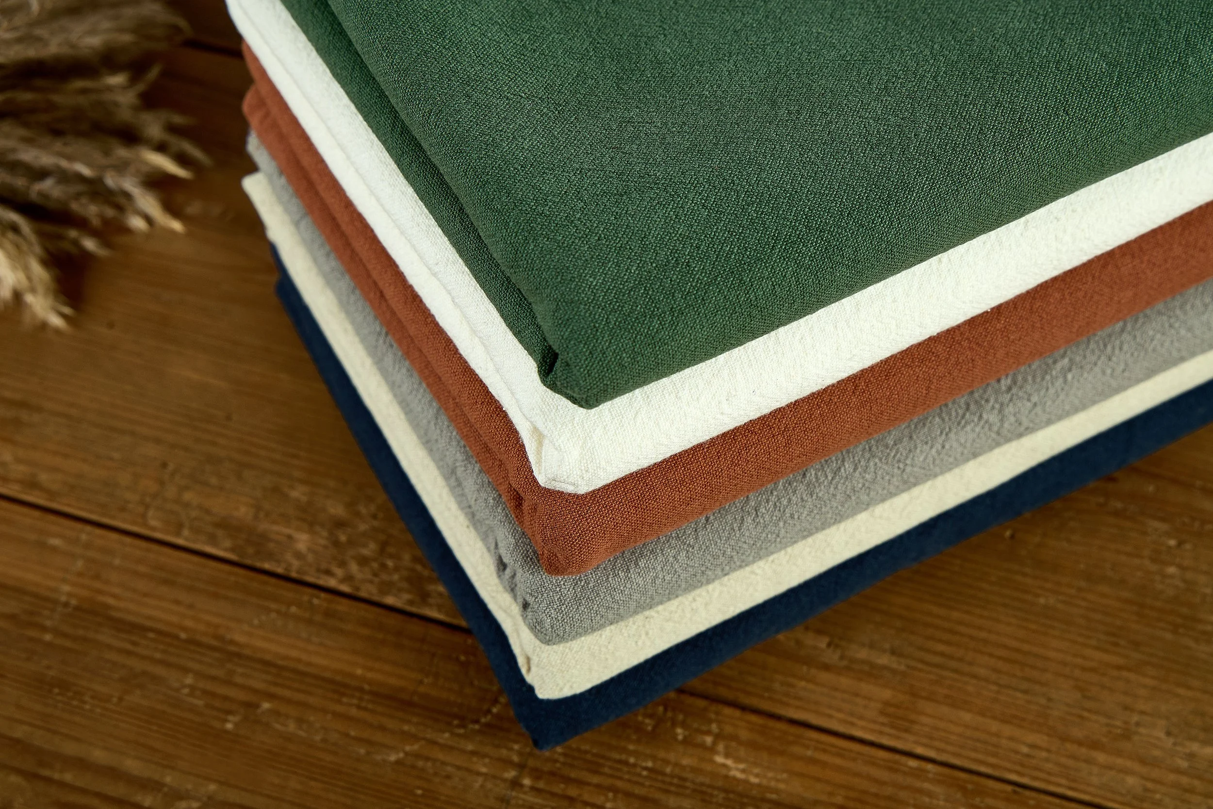 Neatly folded 30 linen 70 cotton blend fabric bolts in multiple earthy colors for wholesale garments.