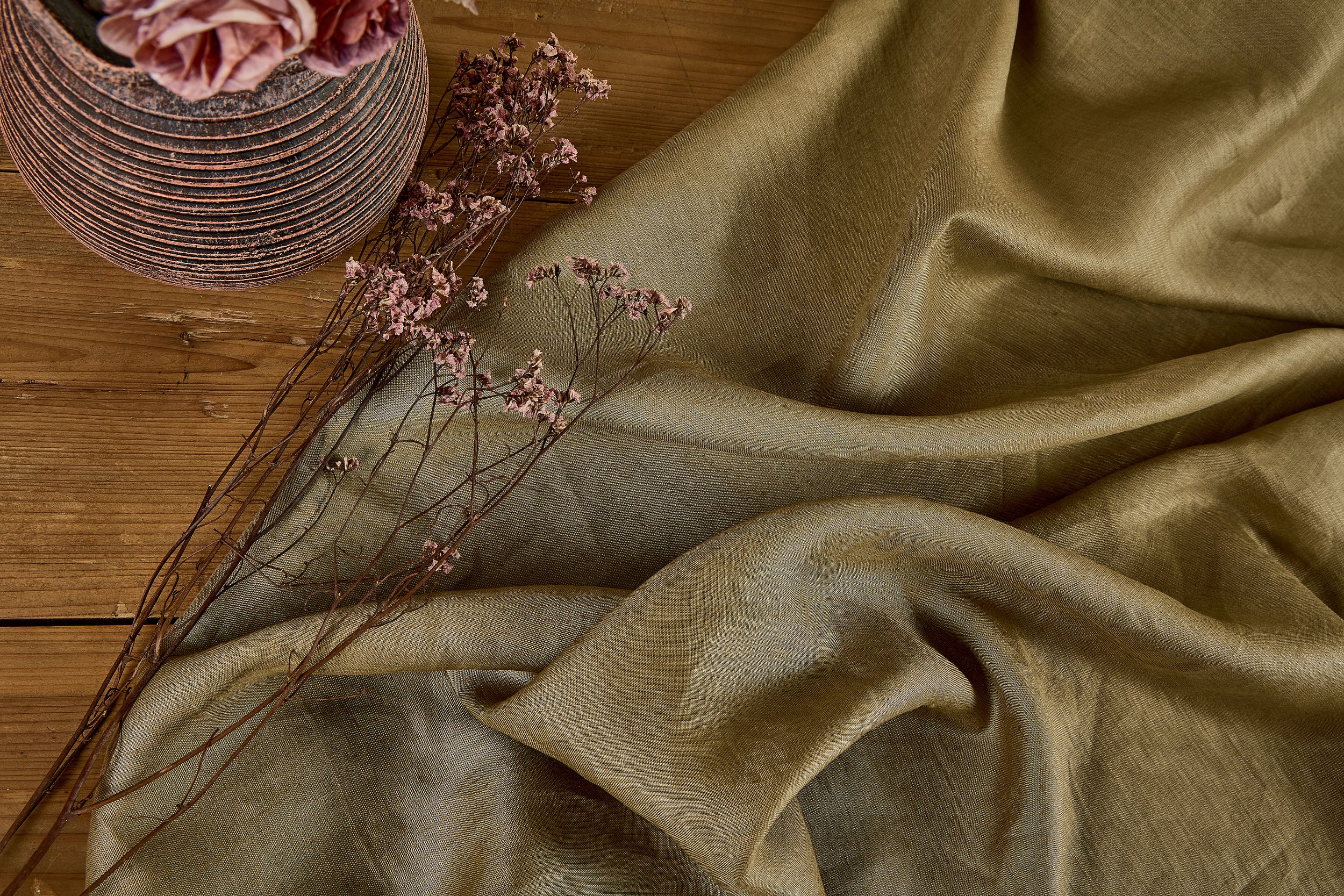 Overhead flat lay of dark green high count pure linen fabric draped over natural rustic wooden table