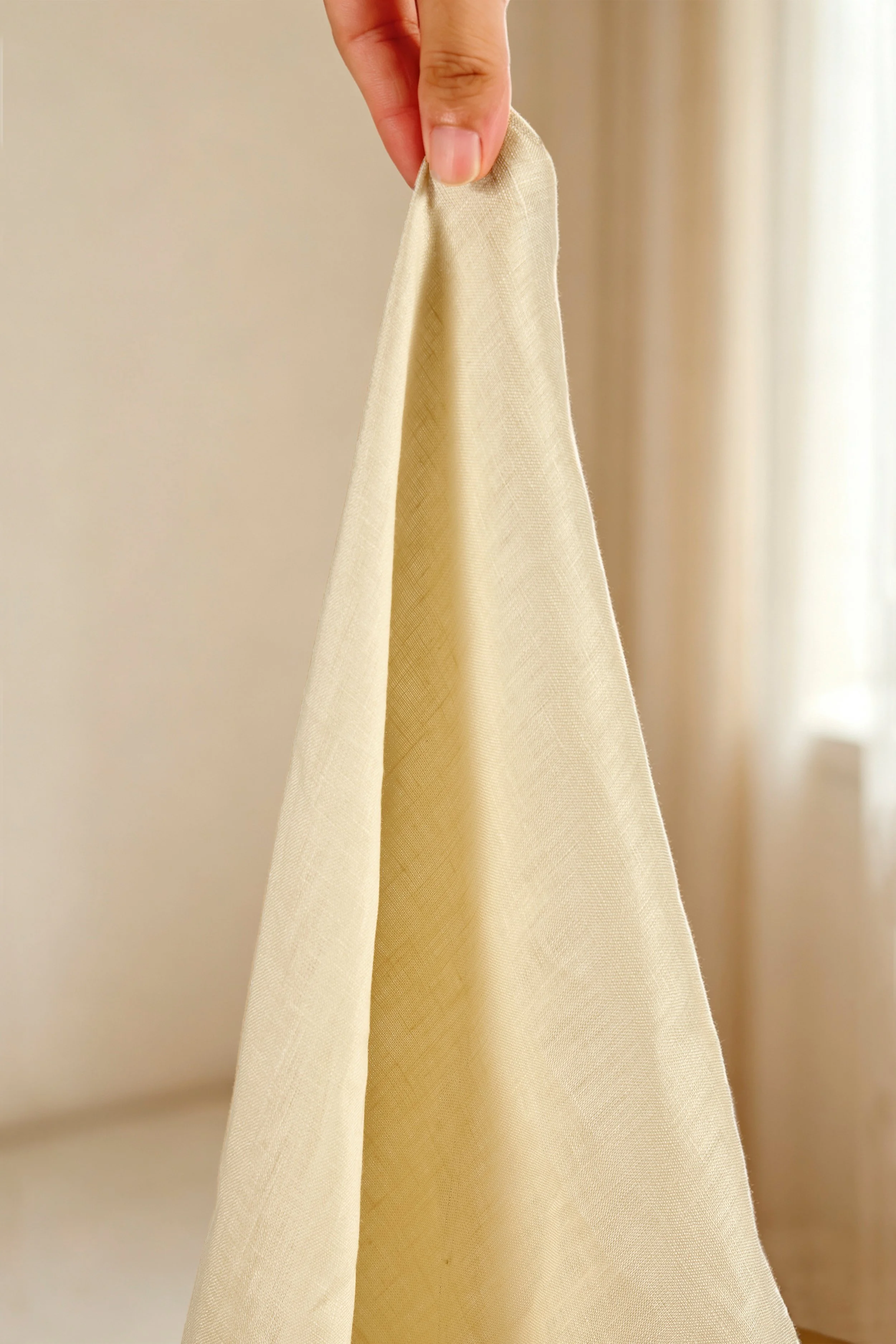 Hand held champagne beige pure linen fabric displaying lightweight semi sheer drape and airy summer weave