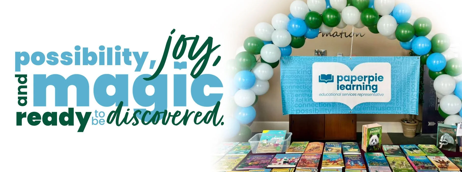 A promotional graphic with the quote 'possibility, joy, and magic to be discovered' on the left side, and a display of books, a blue Paperpie Learning sign, and a balloon arch in green, white, and blue on the right side.