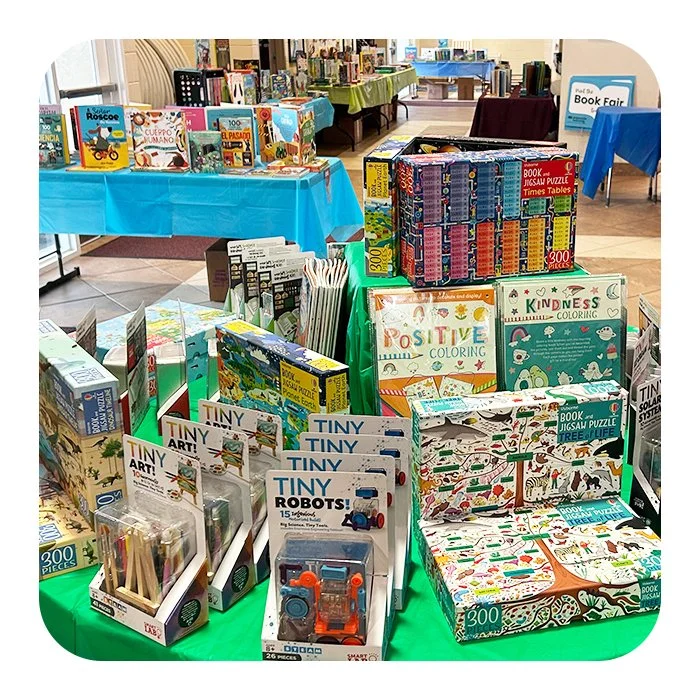 Display of children's books, puzzles, art kits, and toys on tables at a book fair.