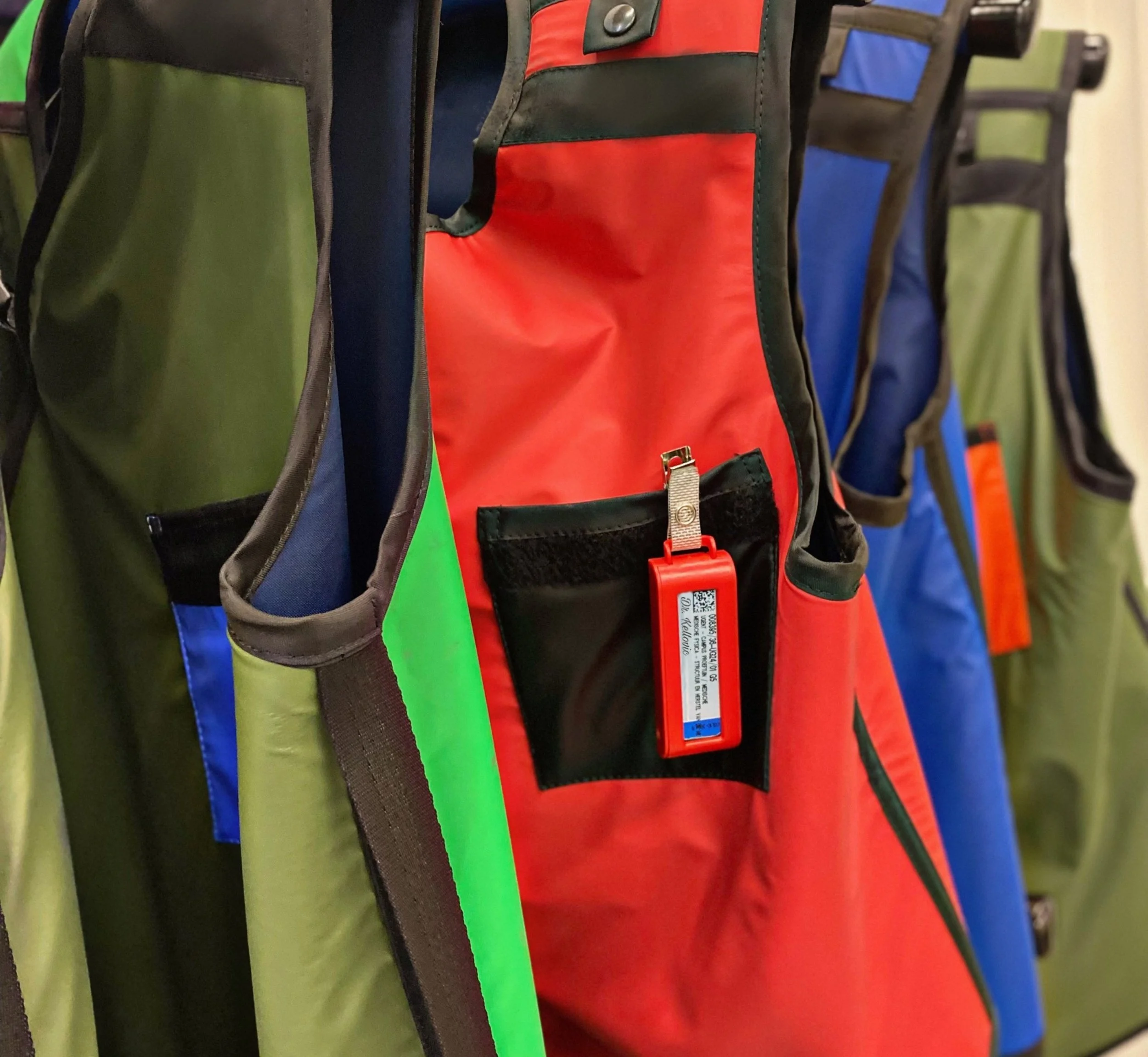 Een rij kleurrijke rugzakken in groen, blauw, rood en zwart hangen aan een stok.