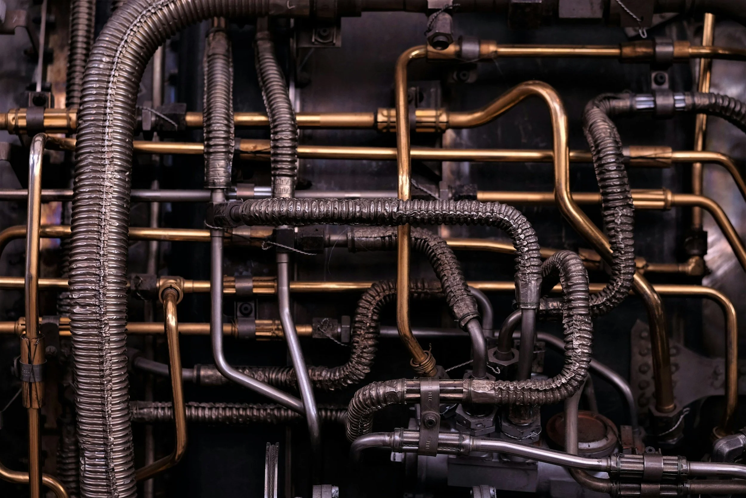 A network of metal pipes and tubes, some are copper and some are steel, in a mechanical or industrial setting.