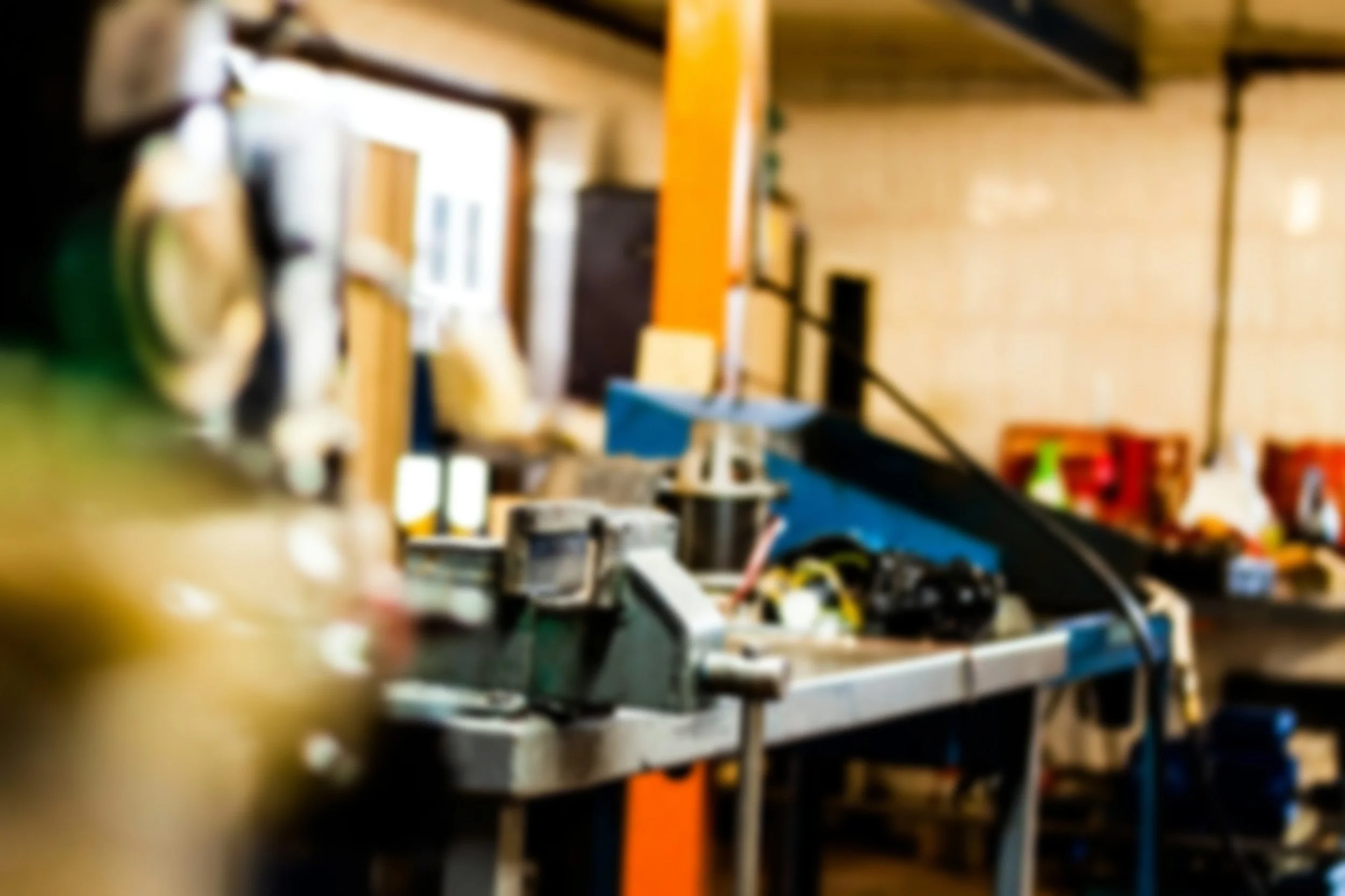 Blurred view of a cluttered workshop or garage with various tools and equipment on shelves and work surfaces.