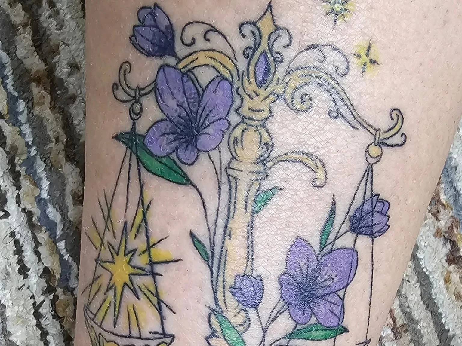 A tattoo of purple butterflies, green leaves, and yellow stars on human skin.