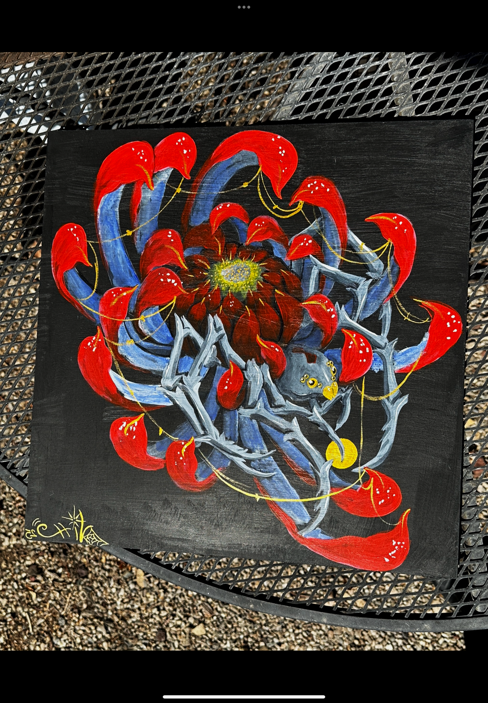 A painting of a spider with red, blue, and gray colors on a black background. The spider has a large, detailed abdomen with a yellow center, and long, thin legs with yellow accents. The artist's signature is in yellow at the bottom left corner.
