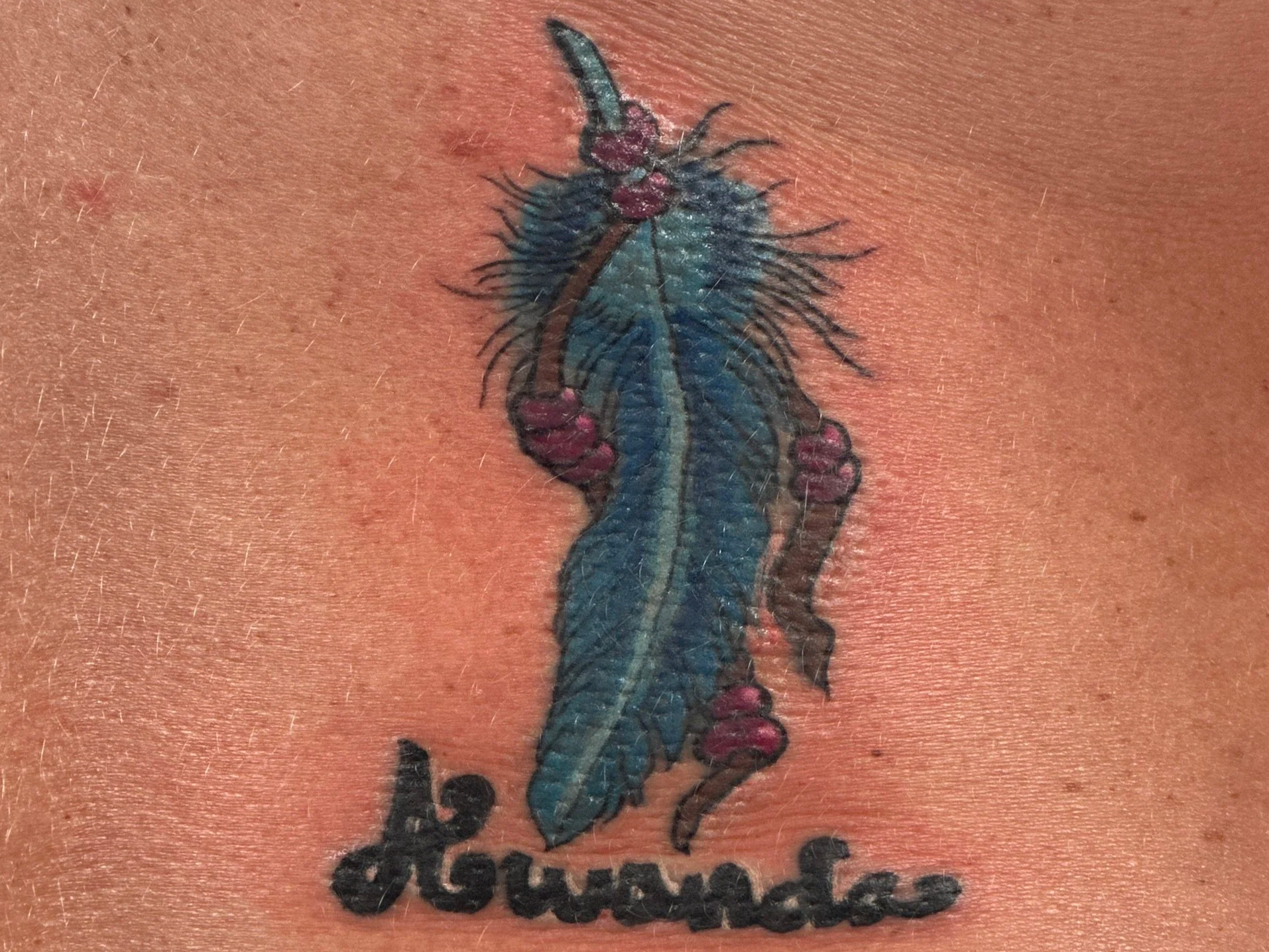 Close-up of a tattoo depicting a blue and green dragon with pink accents, topped with small black symbols.