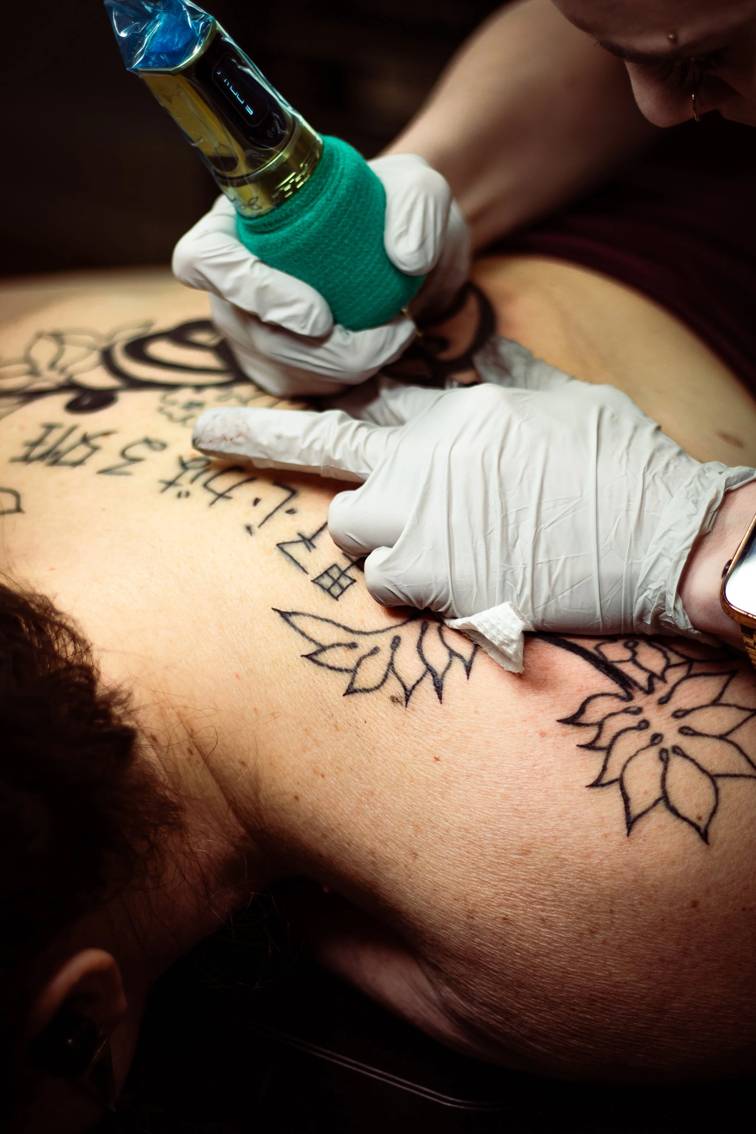 Person getting a tattoo on their side or torso, with another person holding a tattoo machine and wearing gloves.