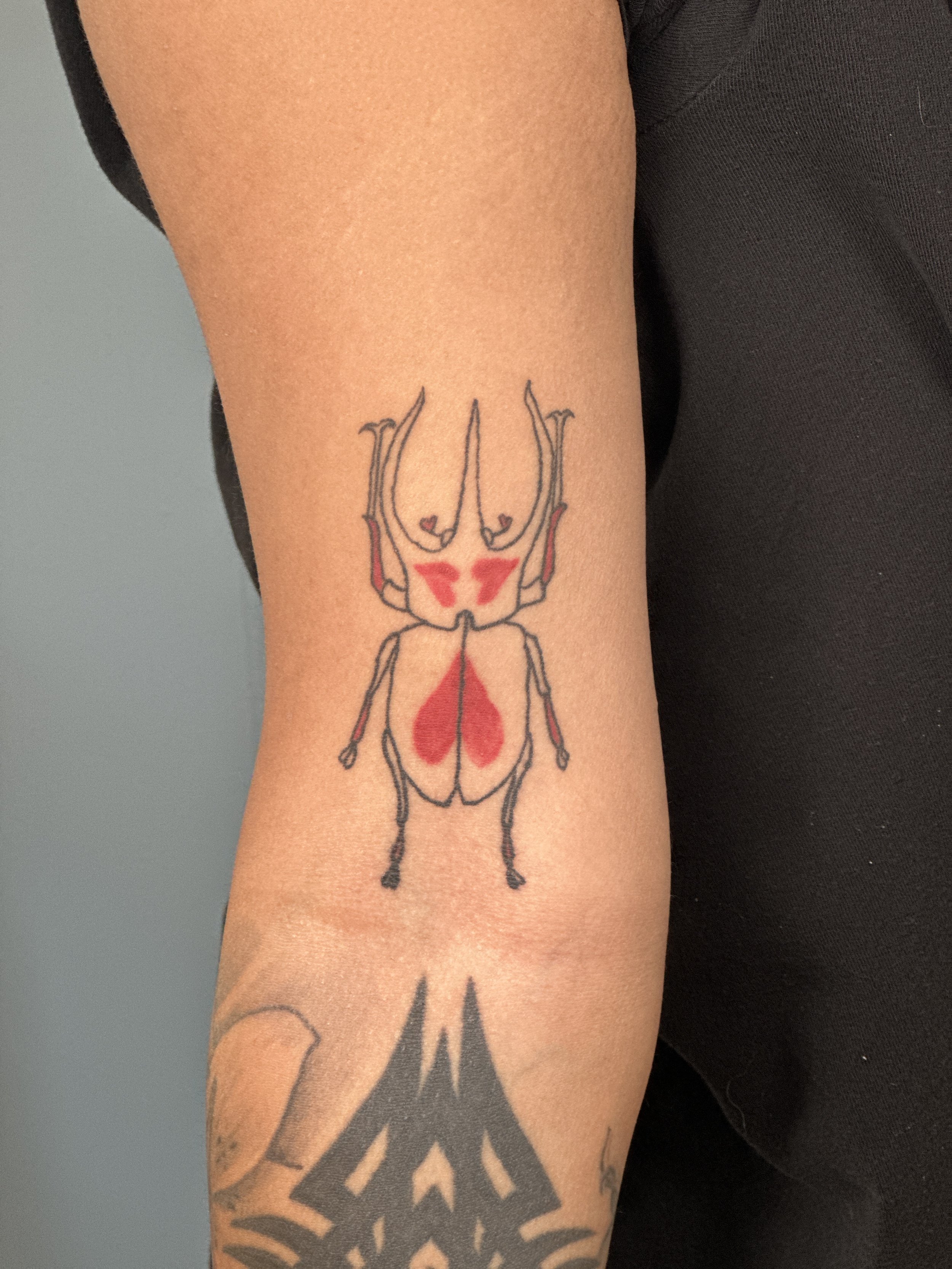 A tattoo of a black line drawing of a skull with red accents on a person's upper arm.