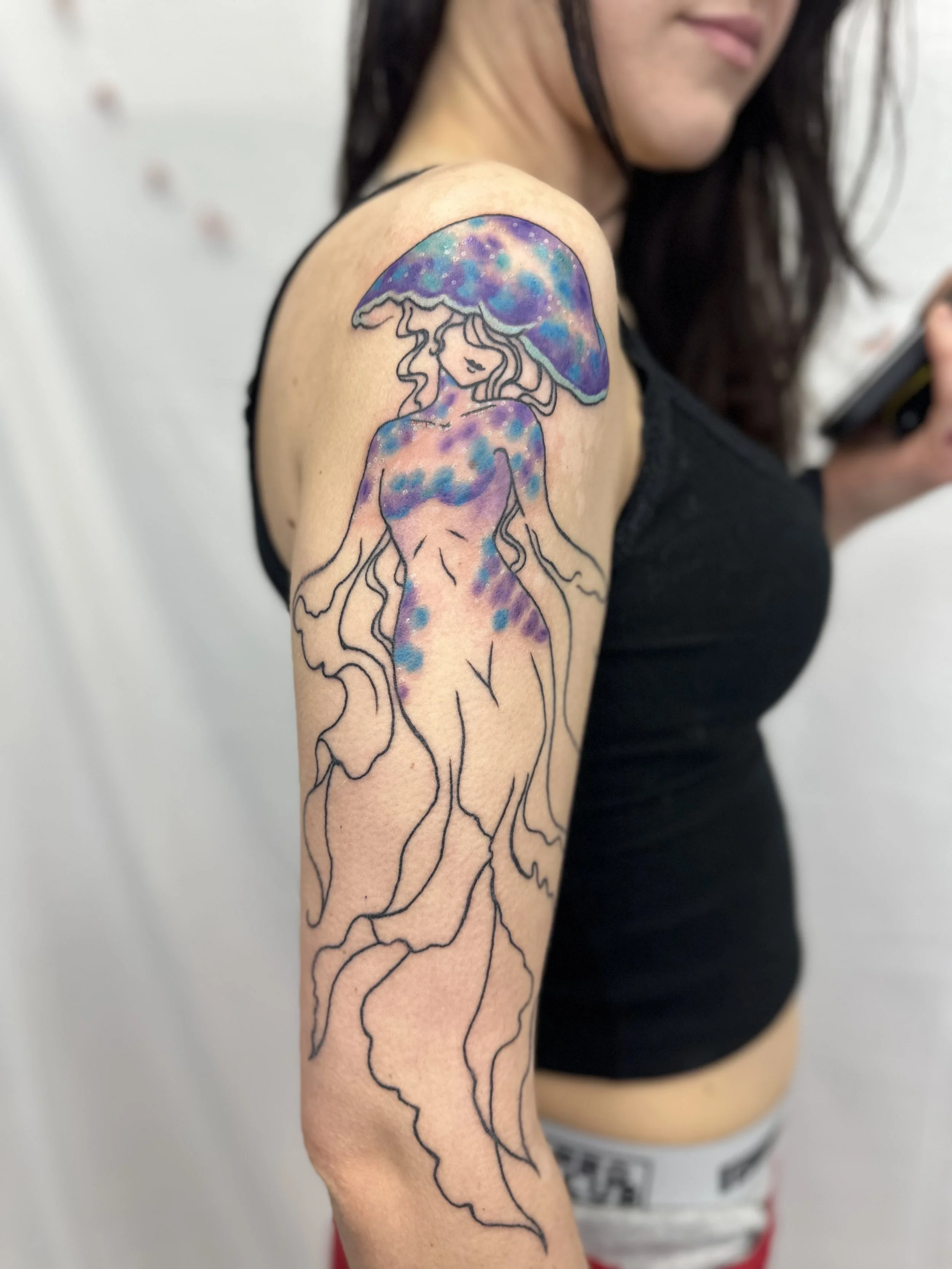 Tattoo of a girl with ocean-colored hair and a mushroom-shaped hat on her shoulder, with a colorful galaxy theme, outlined with black lines.